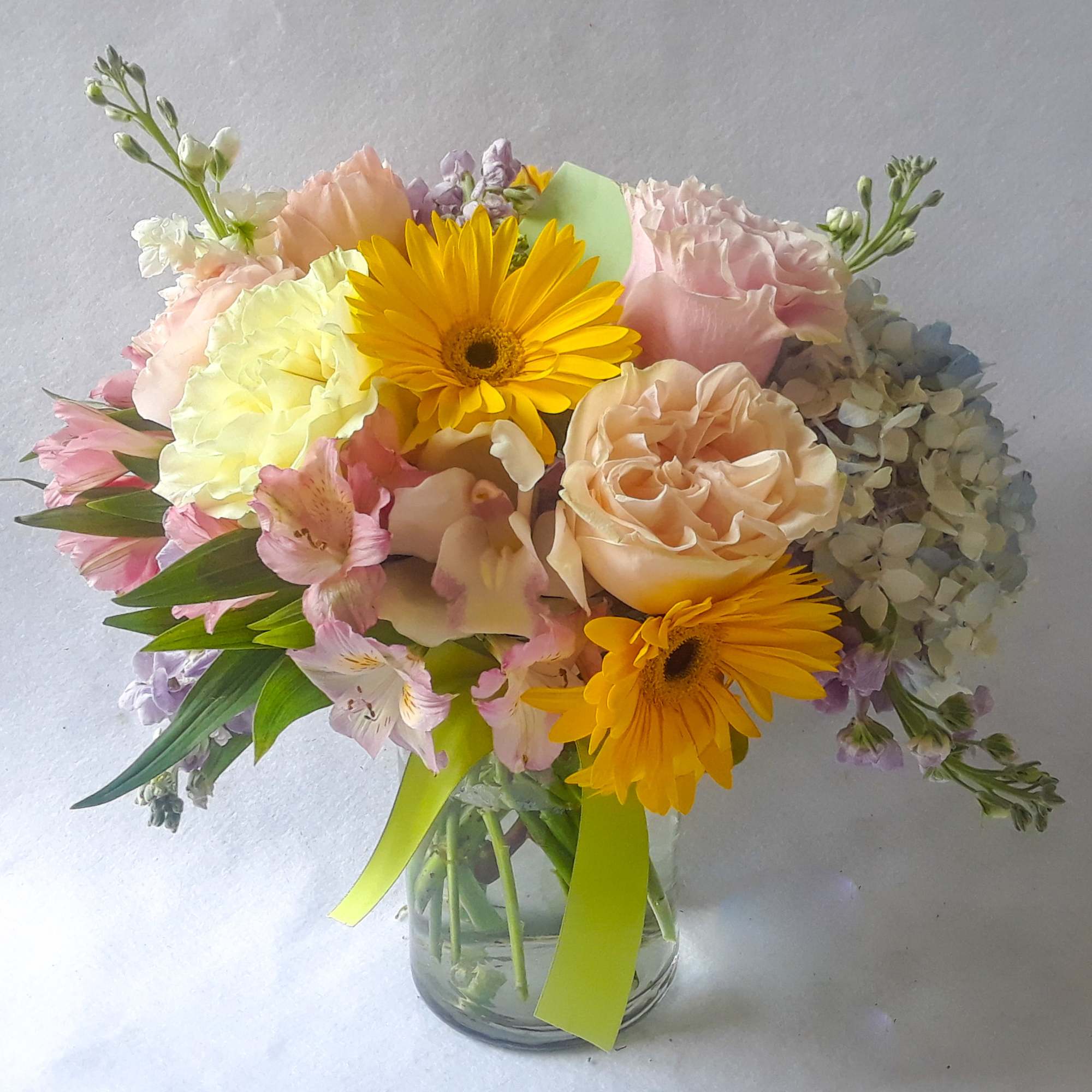 Roses orchids  and more arranged in a tall modern glass cylinder