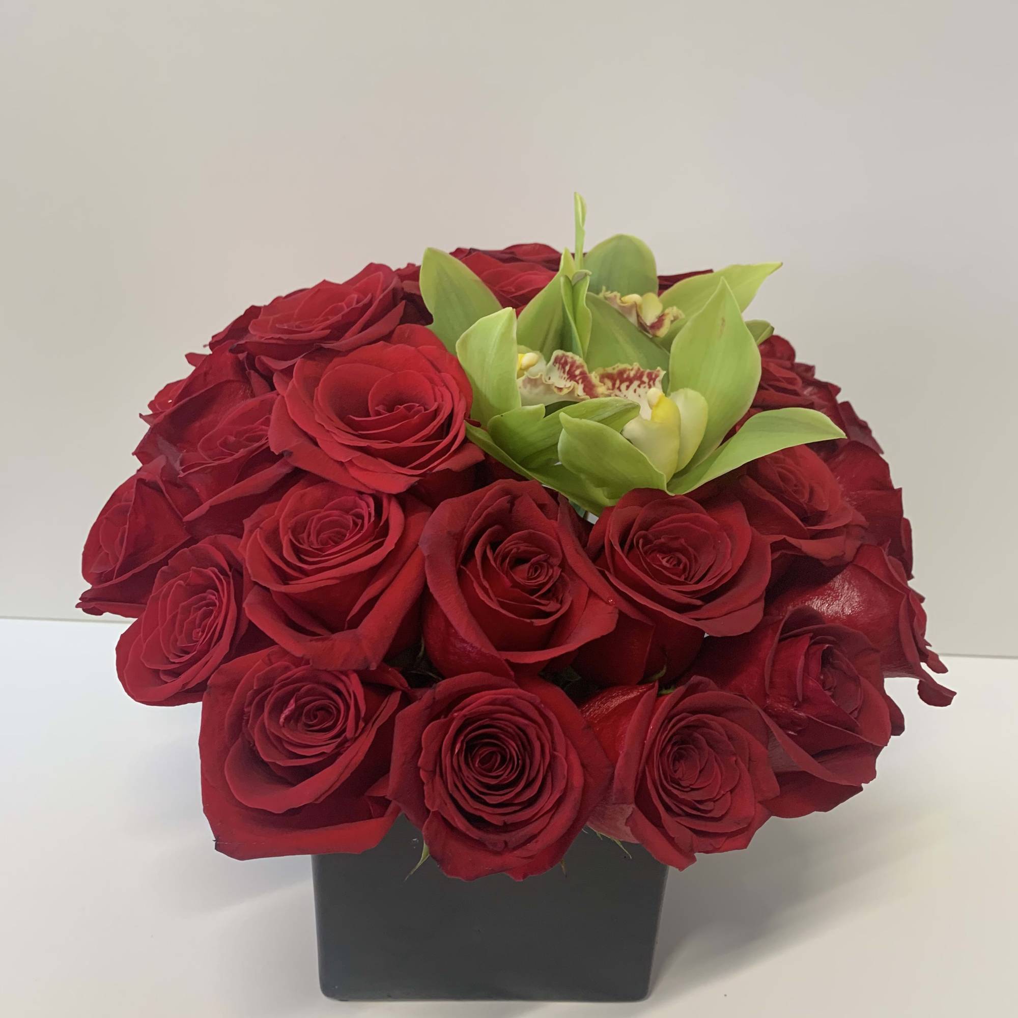 A beautiful arrangement with red roses and green orchids and a black