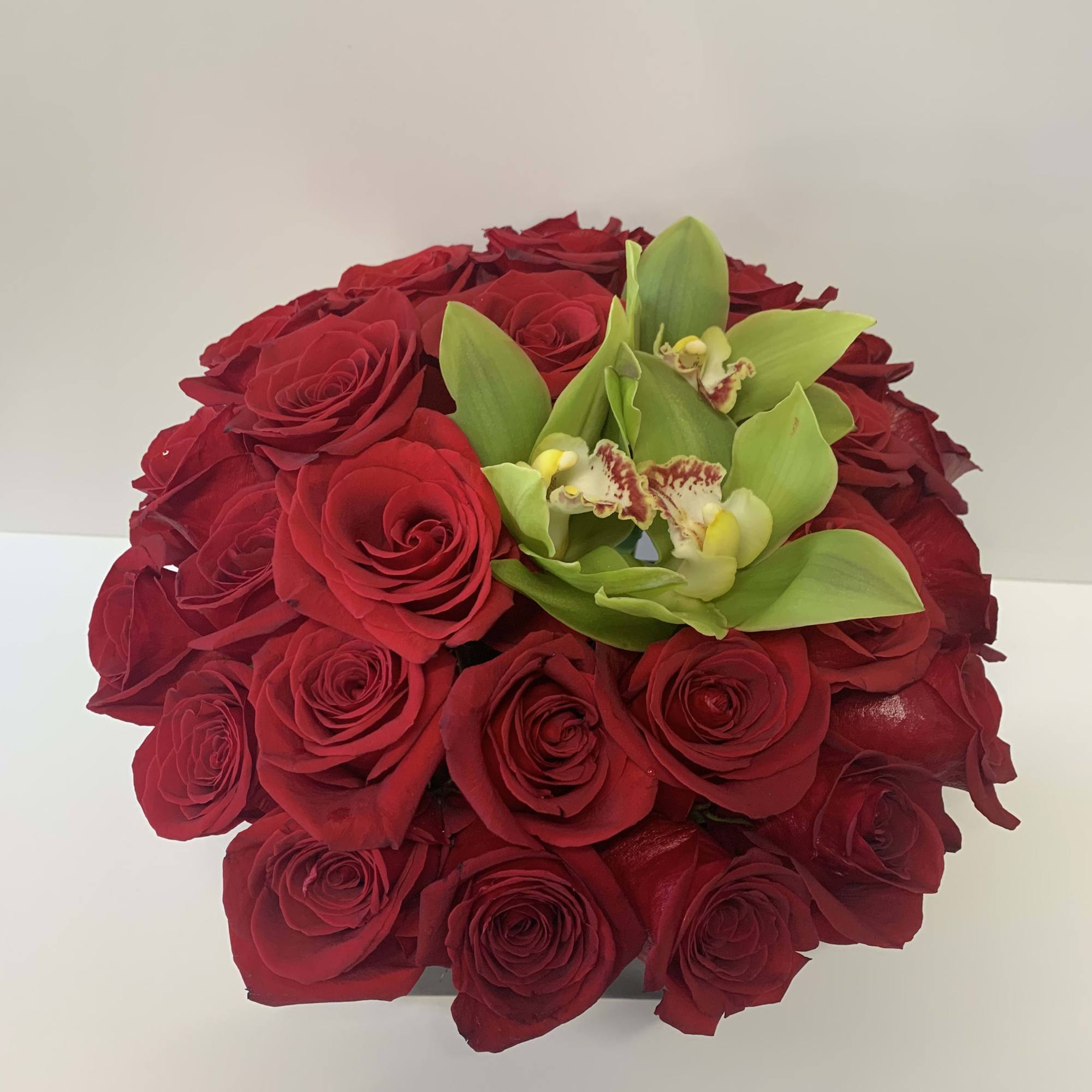 A beautiful arrangement with red roses and green orchids and a black