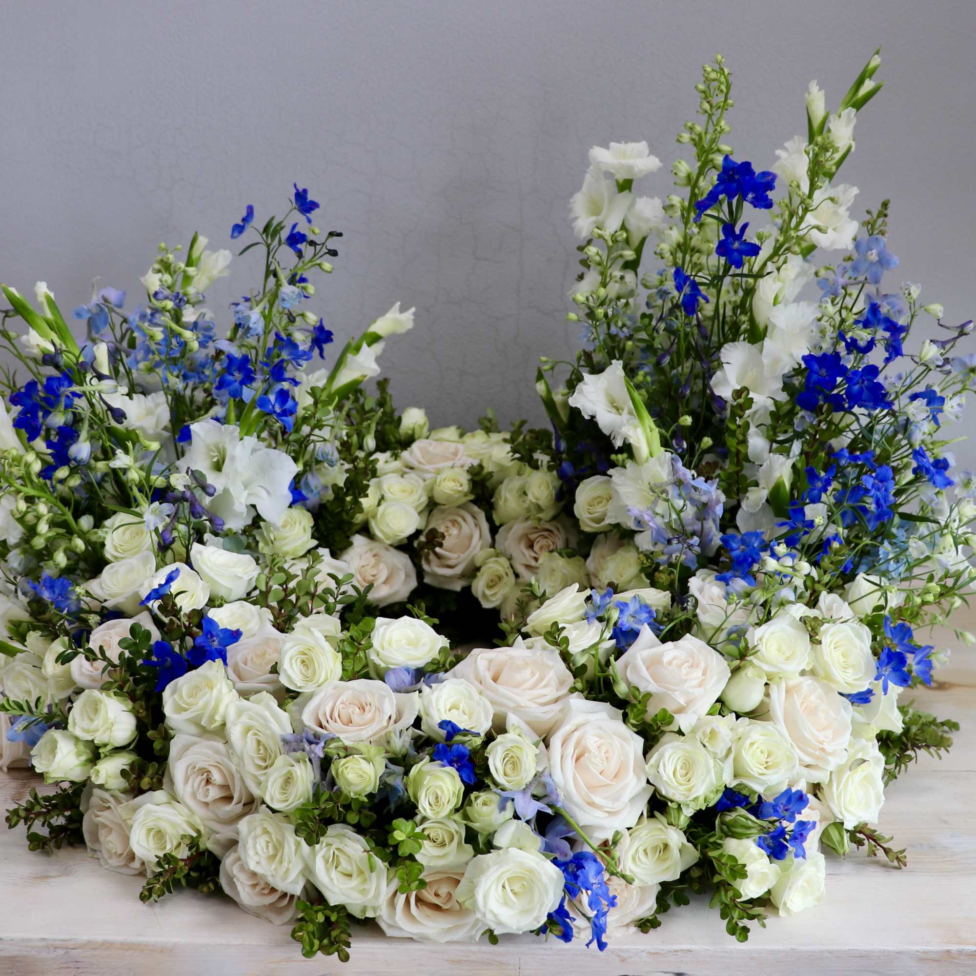 This urn tribute wreath includes a mix of flowers, roses, and seasonal