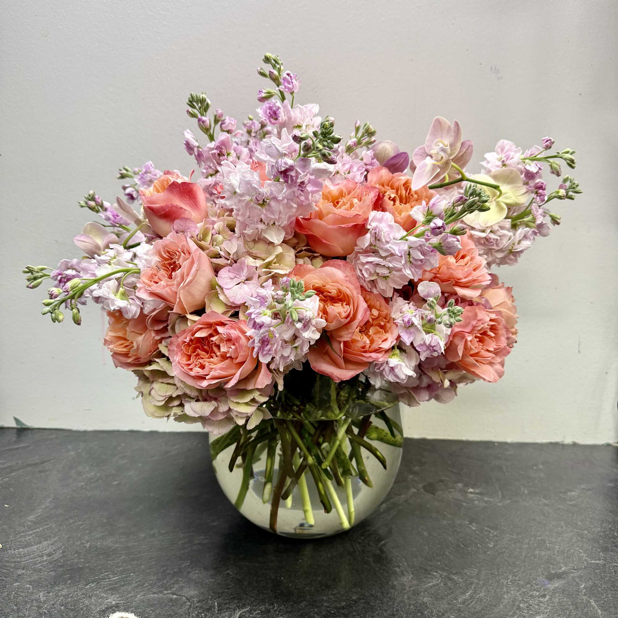 This charming arrangement features lush peach garden roses paired with delicate pink This charming arrangement features lush peach garden roses paired with delicate pink
