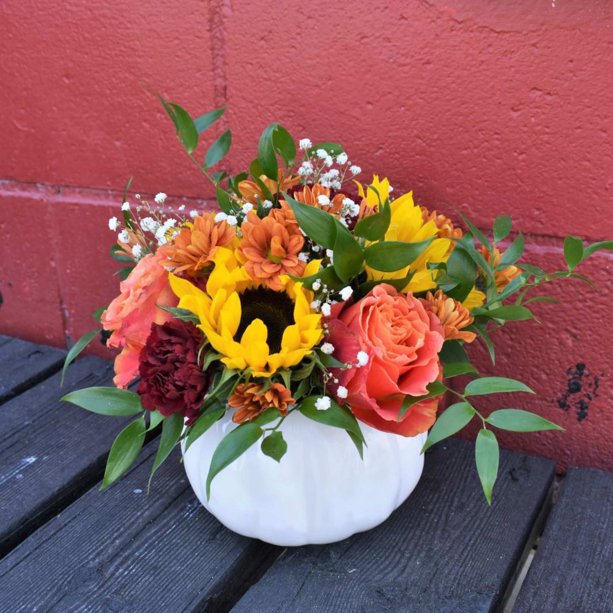 Bright sunflowers, orange roses, mums and carnations are designed in a white