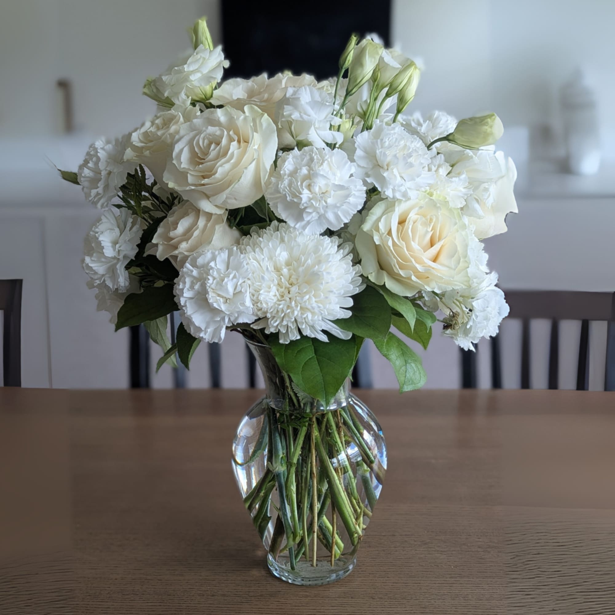 Pure Grace is a timeless white arrangement featuring roses, carnations, lisianthus, and