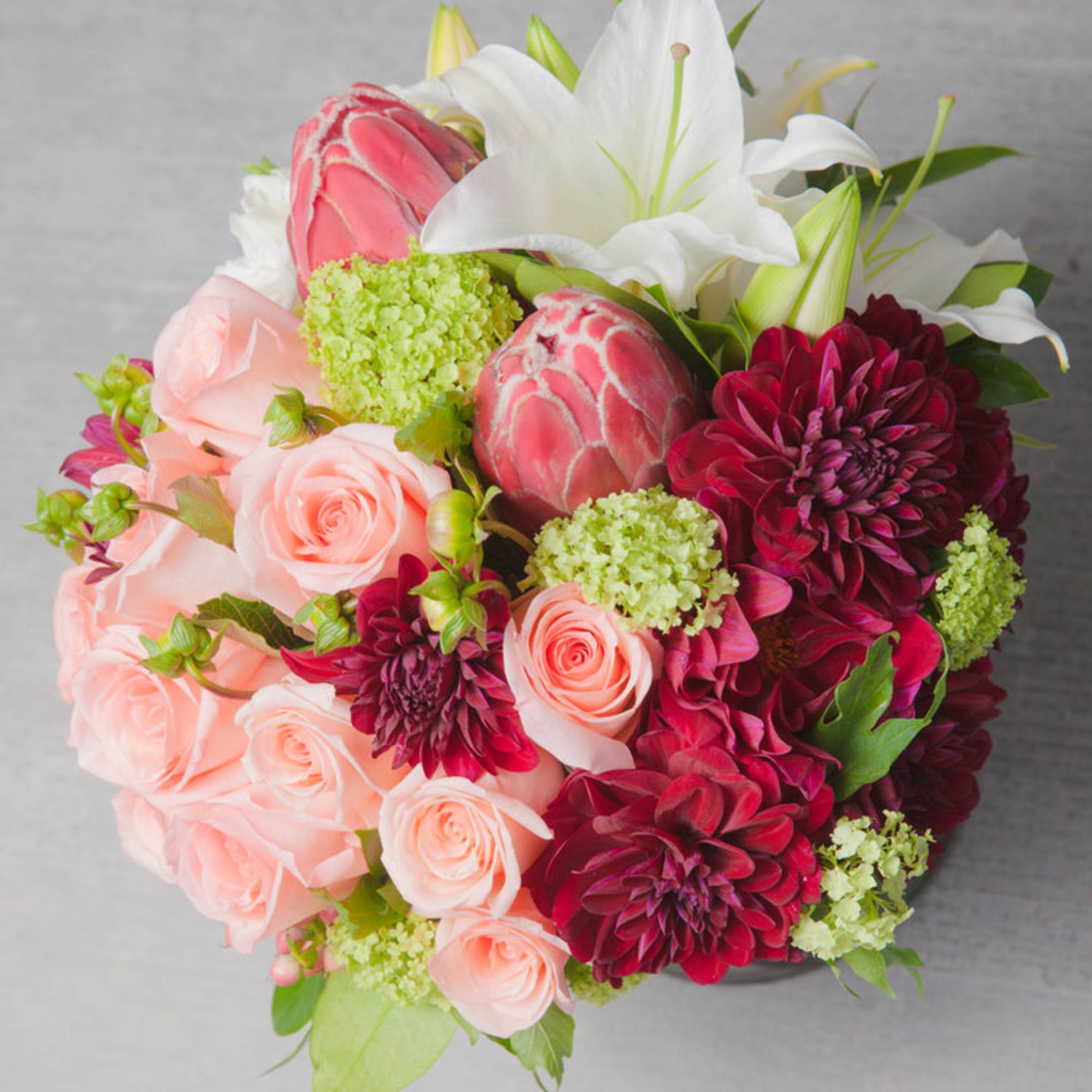 A modern composition of dusty pink Roses, rhubarb red tropicals, heirloom tomato-red
