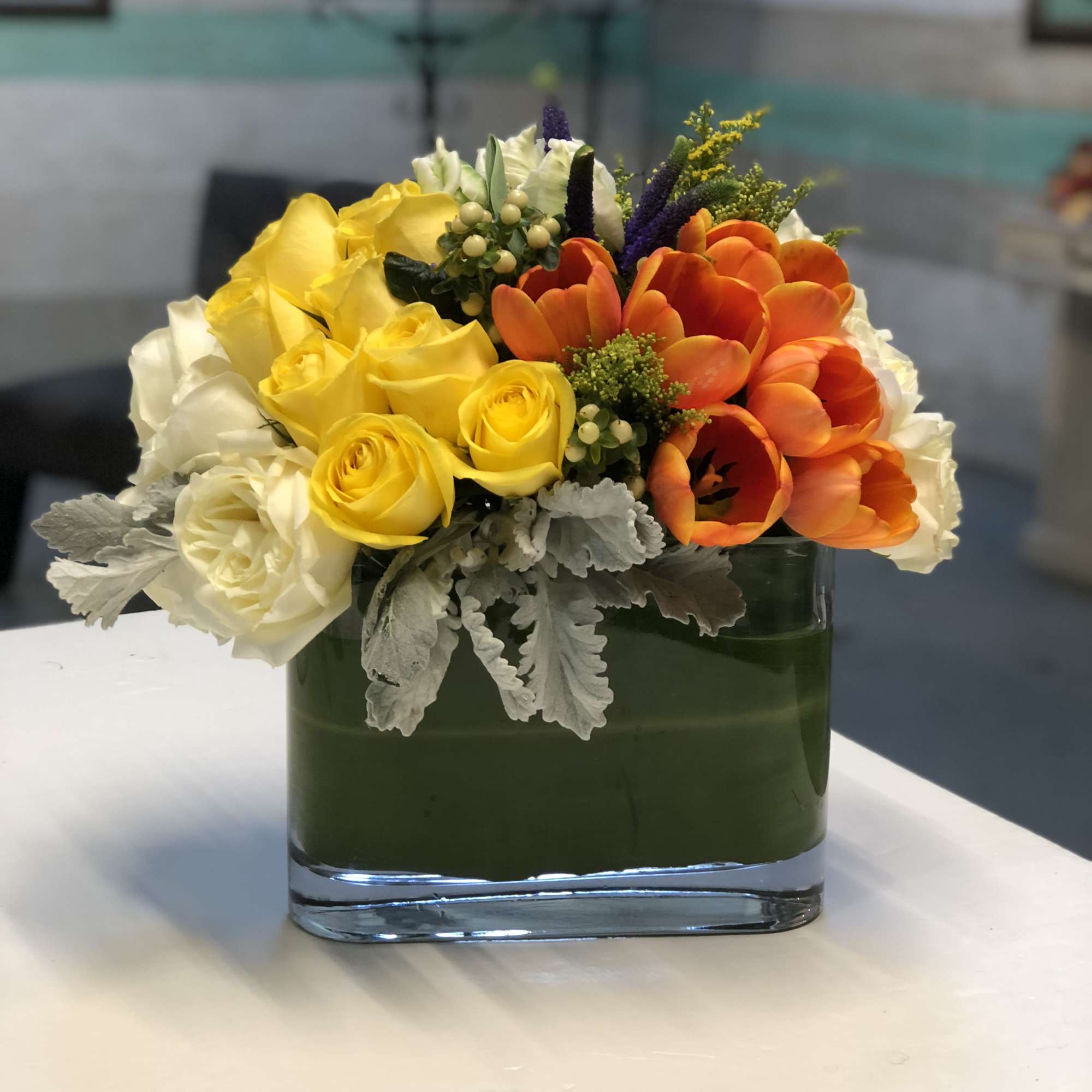 A creative arrangement of papaya-orange Tulips, sunshine-yellow and white Roses, Dusty Miller