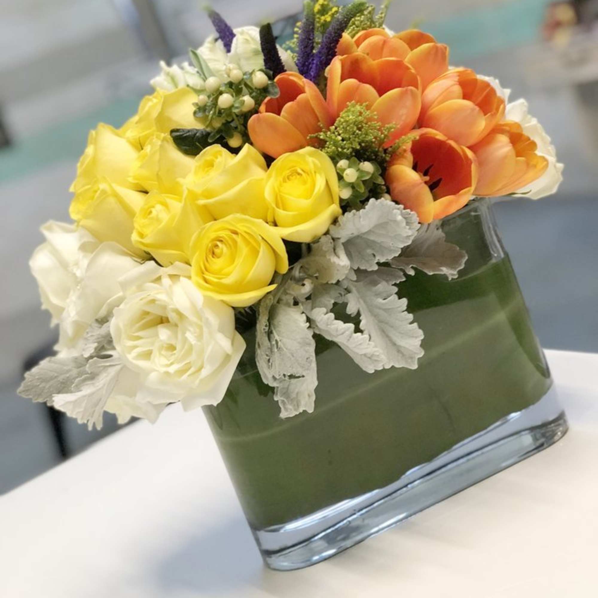 A creative arrangement of papaya-orange Tulips, sunshine-yellow and white Roses, Dusty Miller