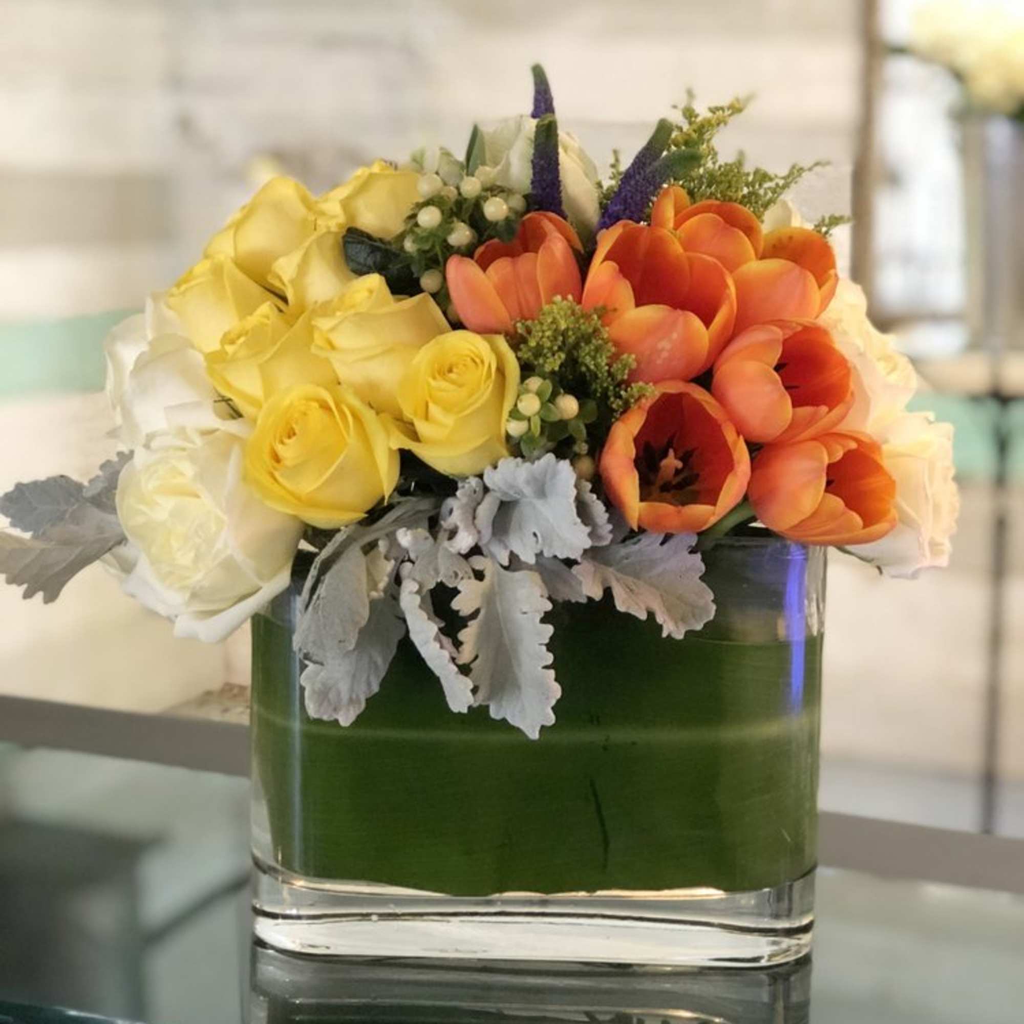 A creative arrangement of papaya-orange Tulips, sunshine-yellow and white Roses, Dusty Miller