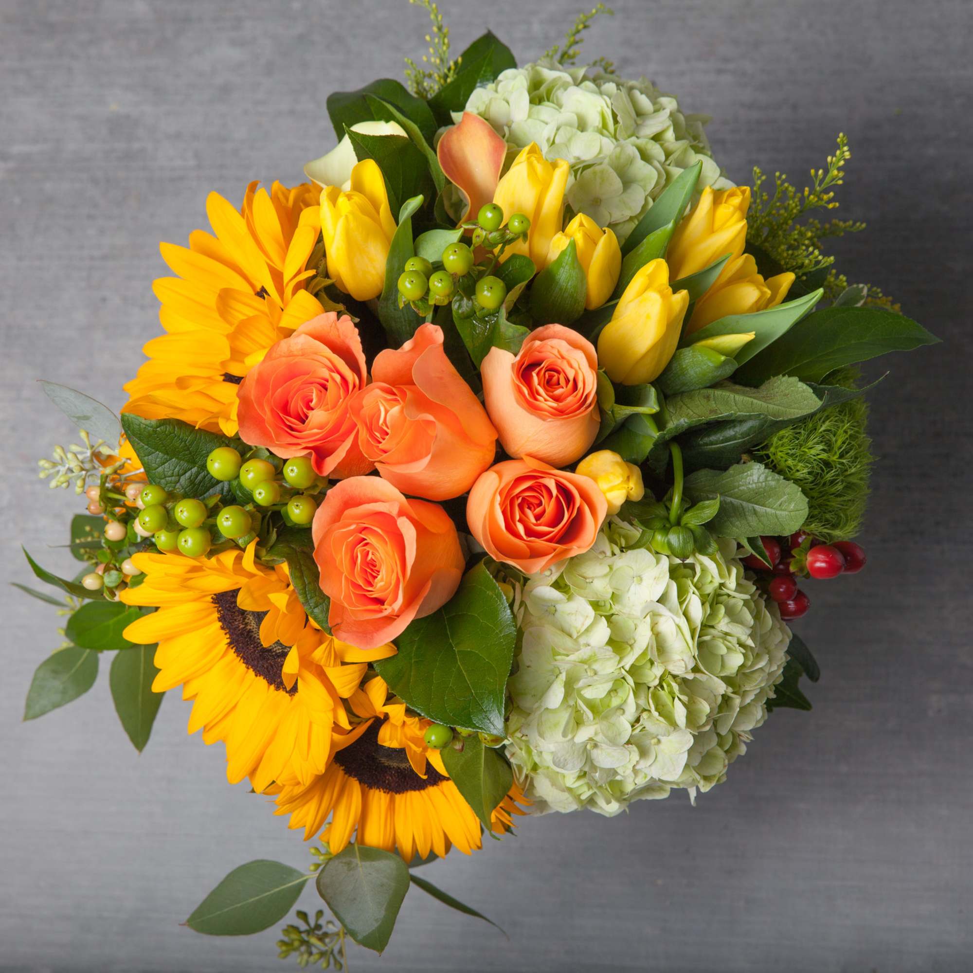 This bountiful arrangement of sunshine creamcicle Roses, banana-toned Tulips, Hydrangeas and brilliant