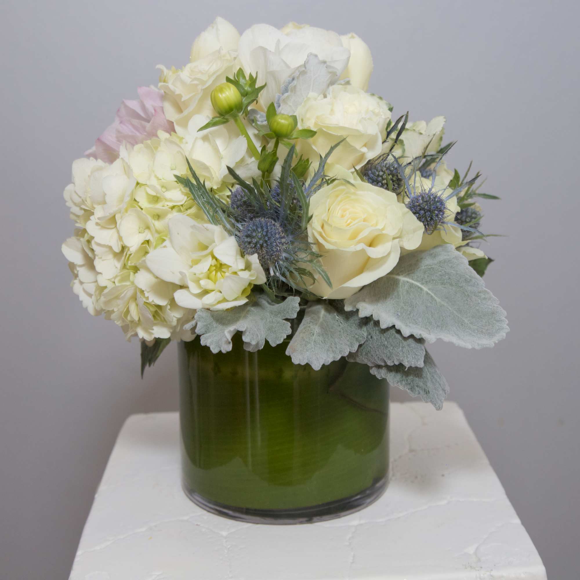 A refreshing arrangement of Snow White Roses and Lilies, frosty succulents framed