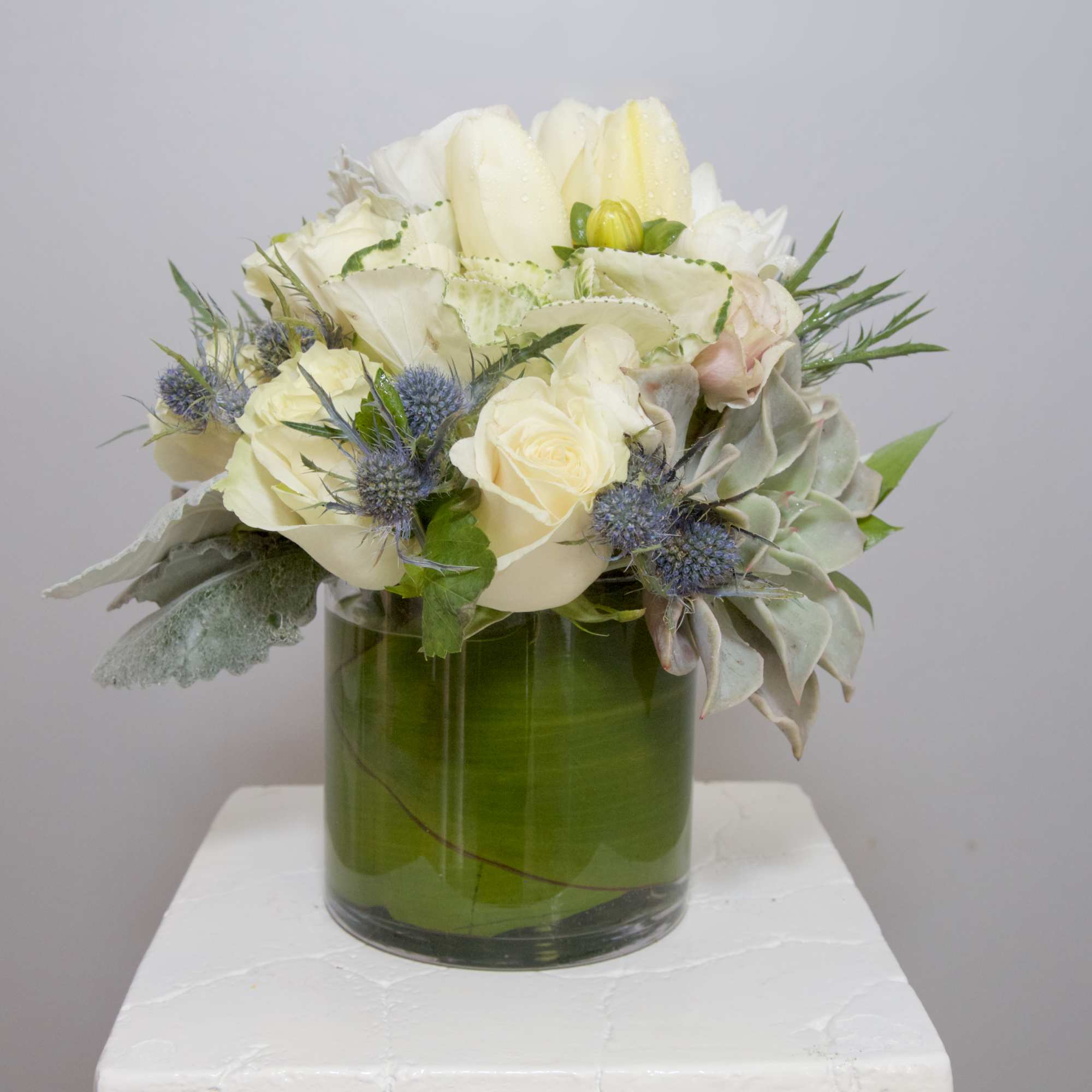 A refreshing arrangement of Snow White Roses and Lilies, frosty succulents framed