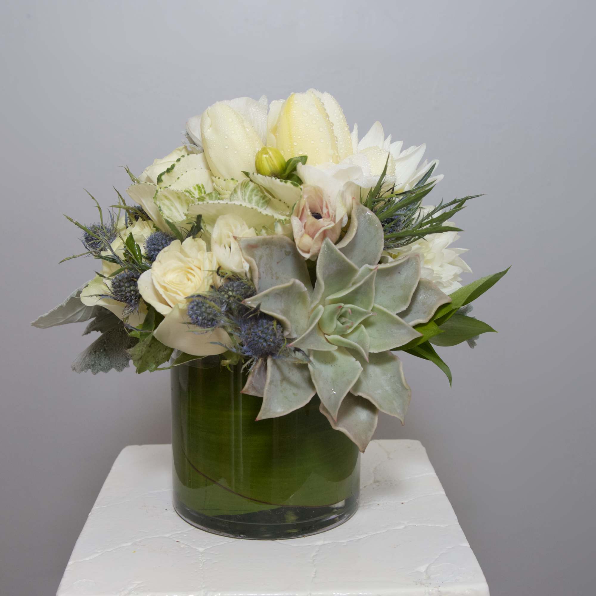 A refreshing arrangement of Snow White Roses and Lilies, frosty succulents framed