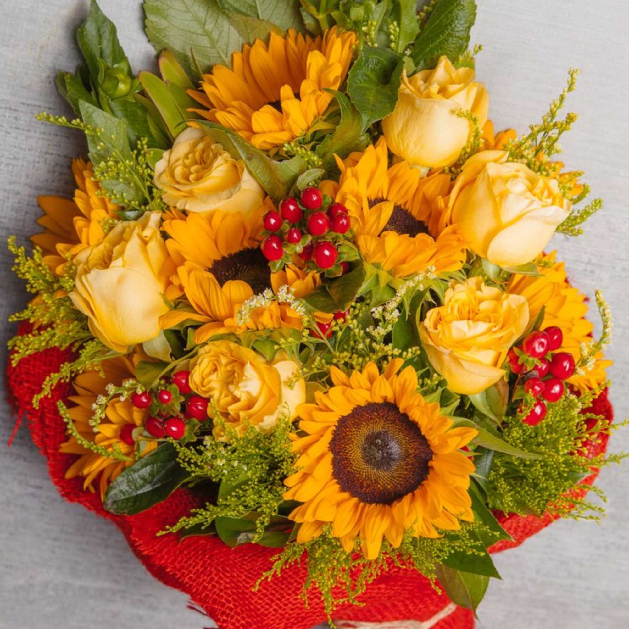 This red burlap wrapped bouquet features delightful Sunflowers, pale yellow Roses, red