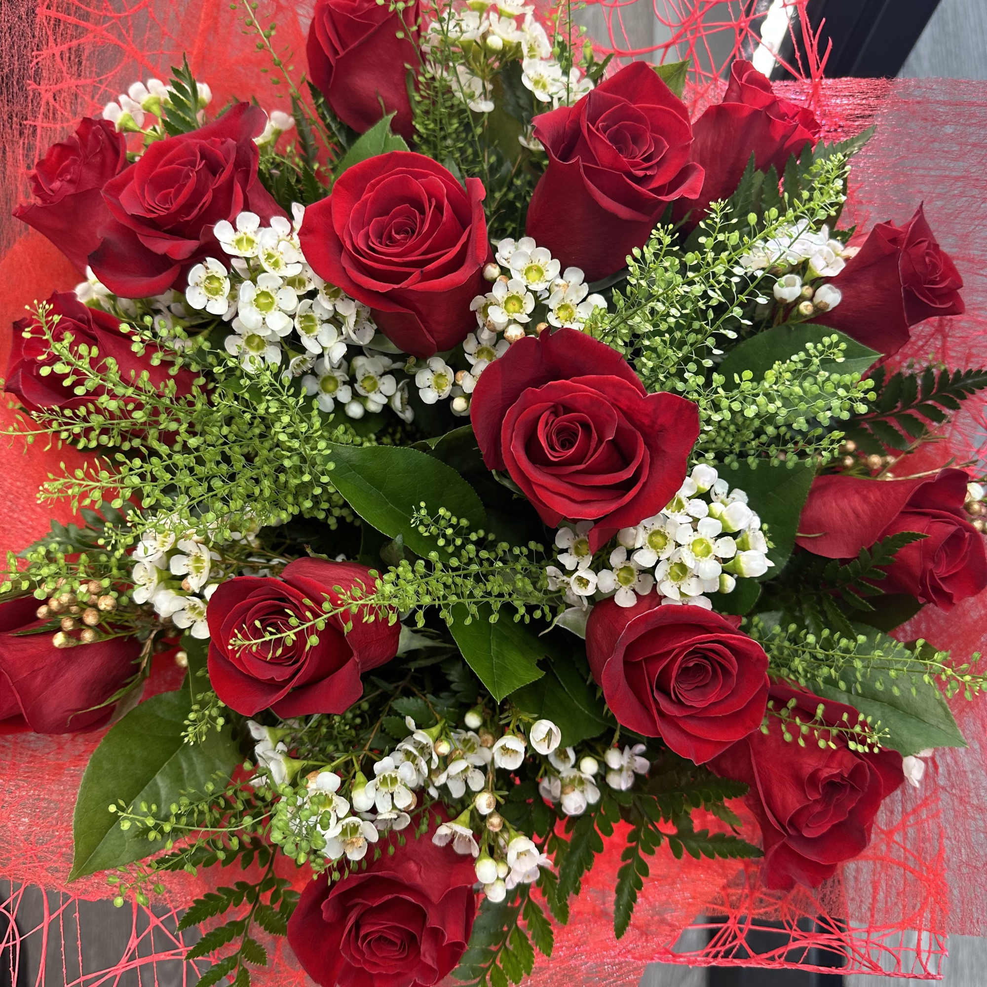 A stunning hand-wrapped bouquet featuring vibrant red roses, delicate white wax flowers