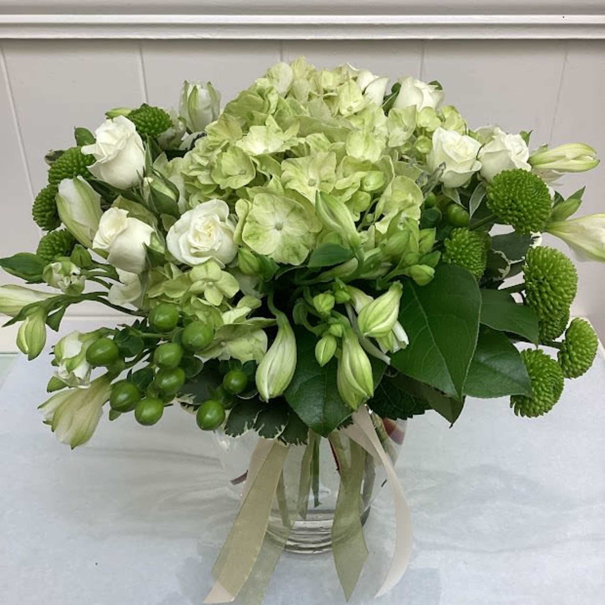 This lusciouss arrangement features green and white flowers. White spray roses complement