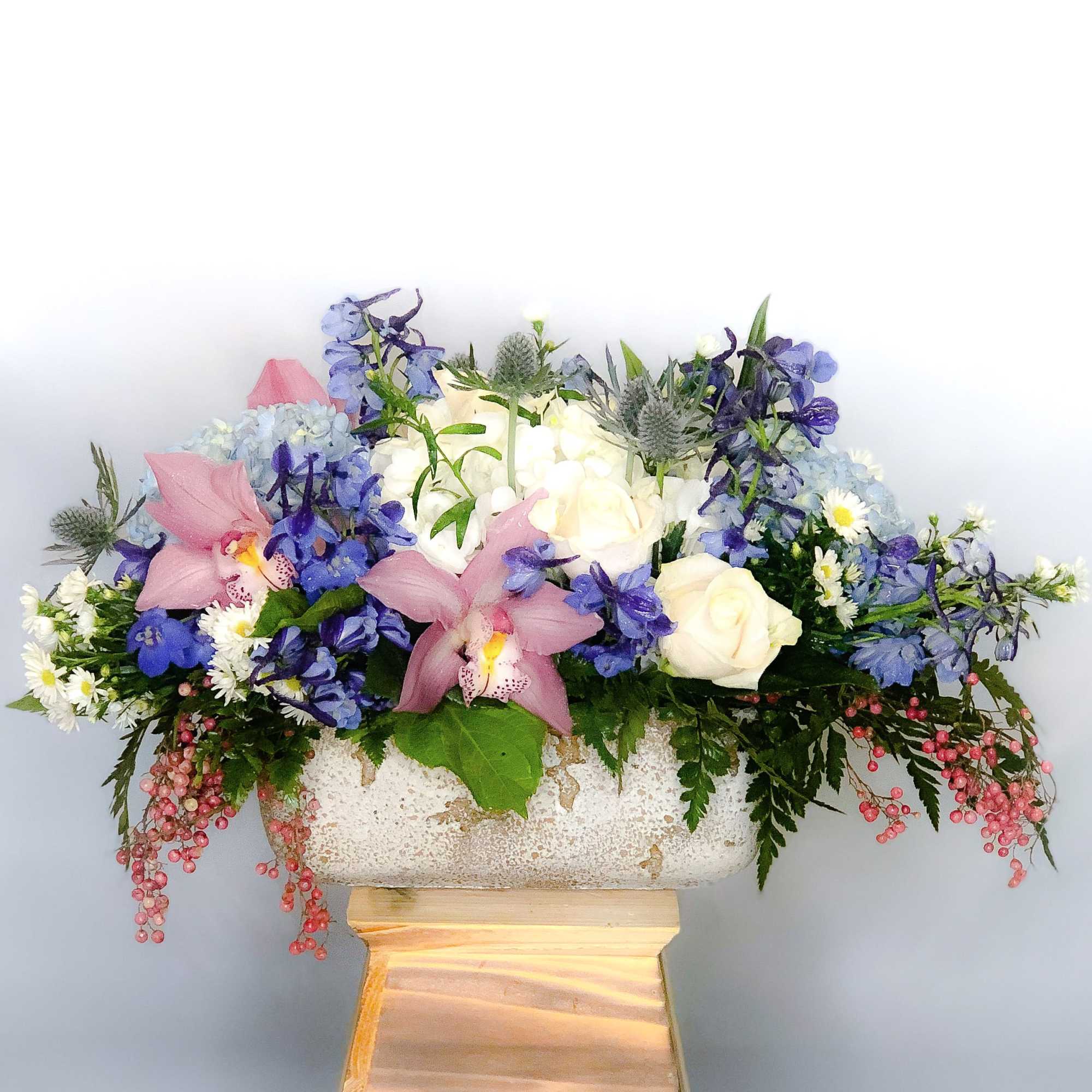 A centerpiece style bouquet elegantly arranged with orchids, hydrangeas, roses and delphinium