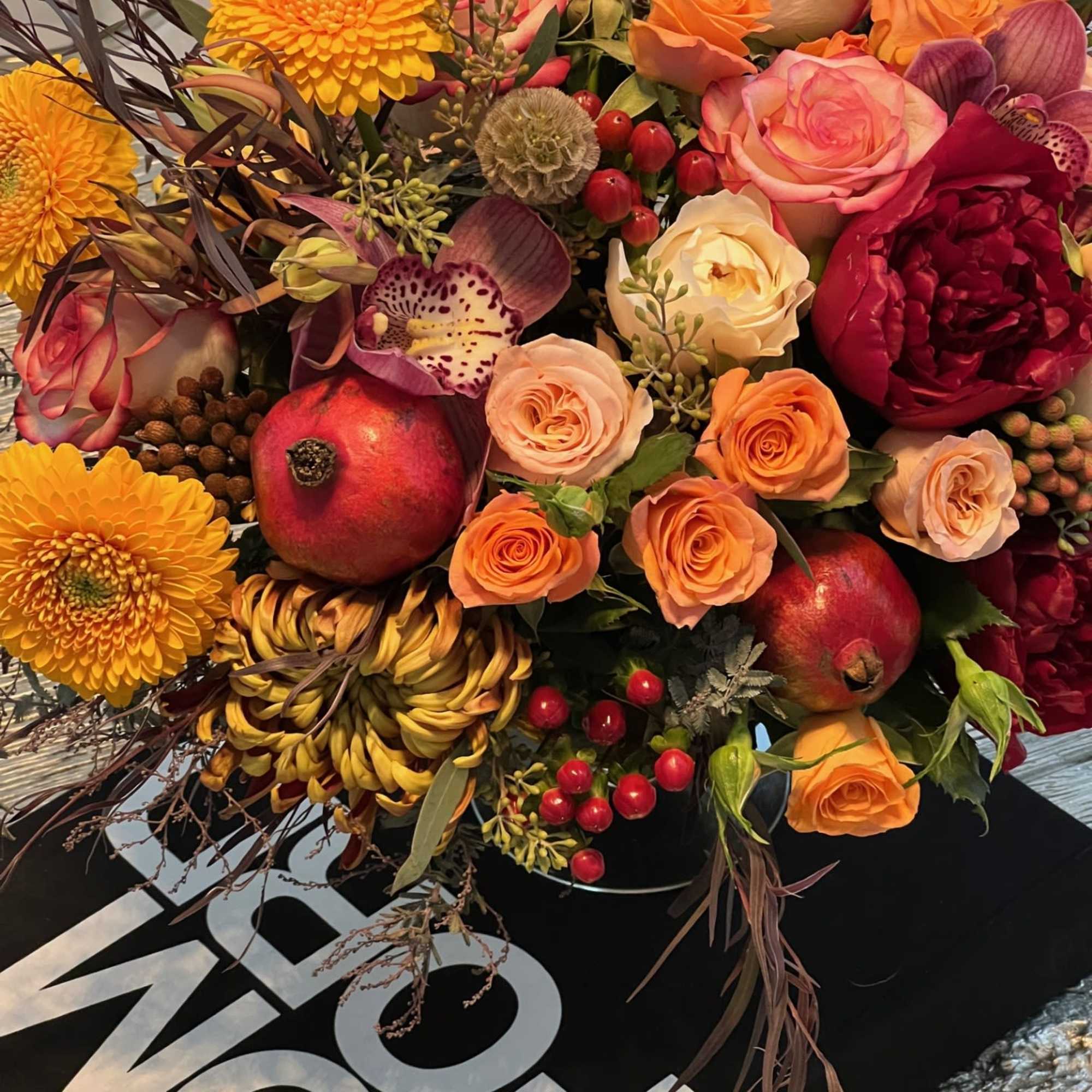 This opulent centerpiece bursts with autumnal charm, blending rich burgundy roses, golden