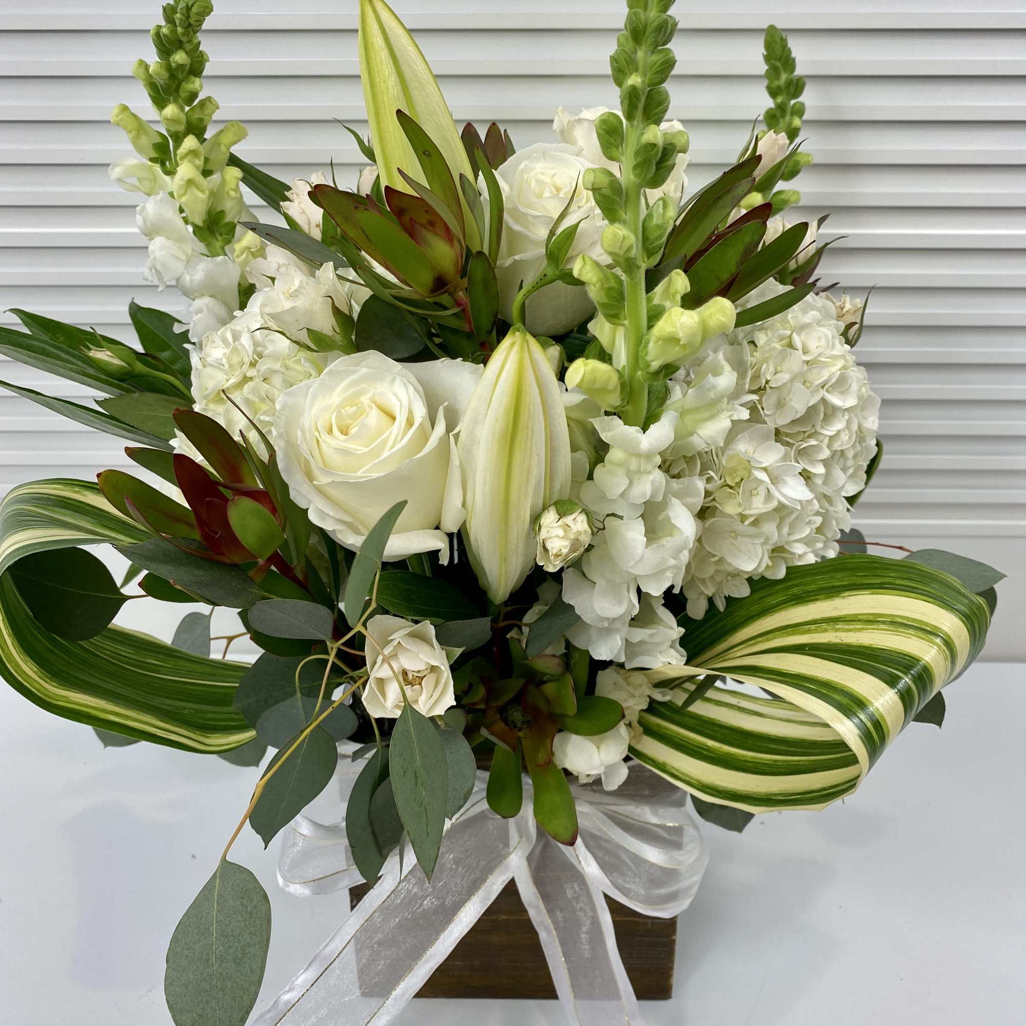 Green and white arrangement in a wooden vase. Hydrangeas, snapdragon, roses and