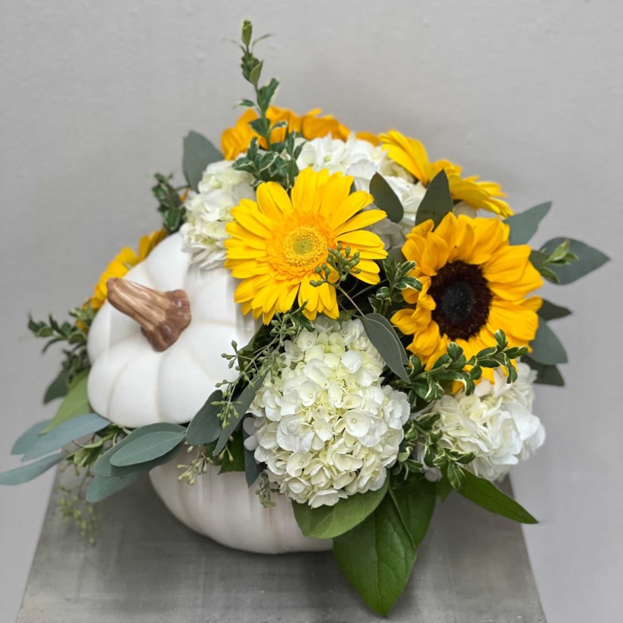 Floral arrangement arranged in a ceramic pumpkin keepsake. White hydrangeas, yellow gerbers