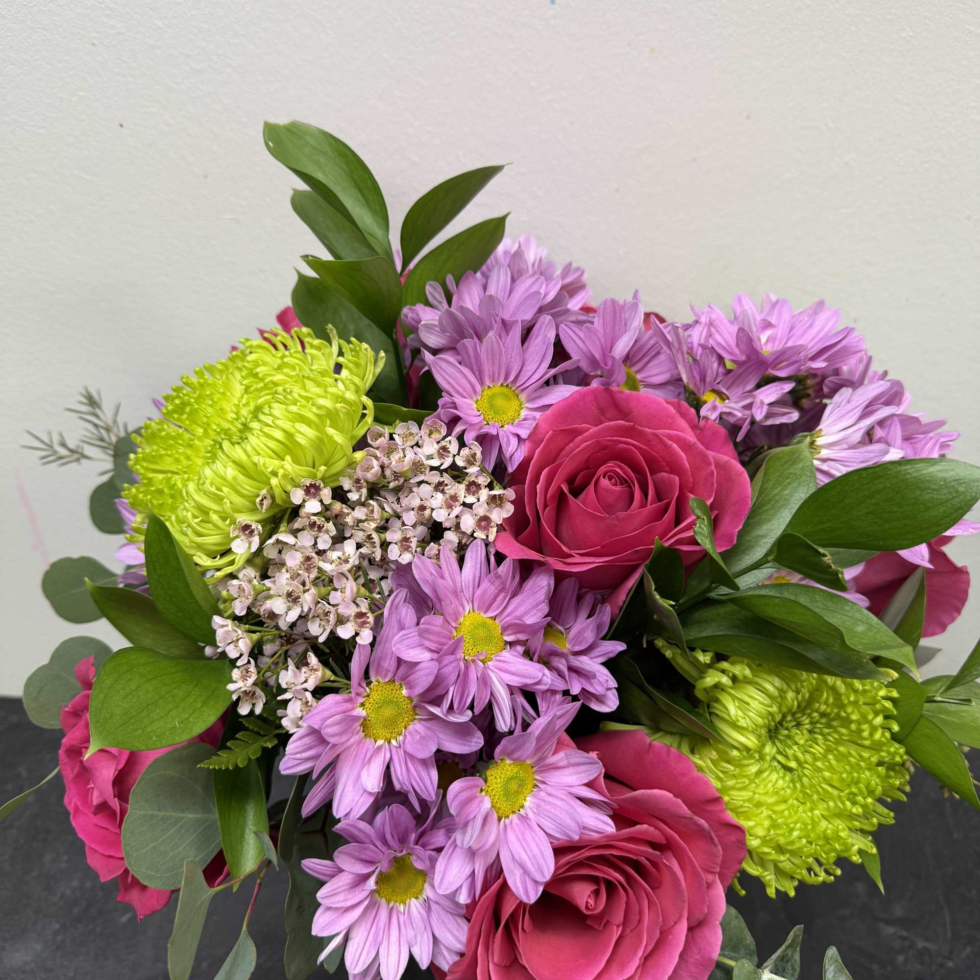 A lively mix of hot pink roses, lavender daisy mums, and bright