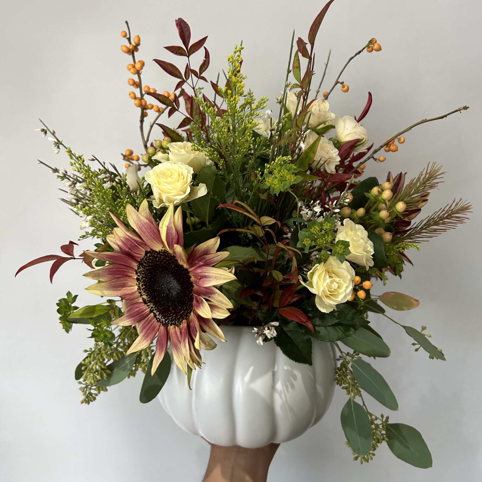 Seasonal flowers arranged into a white pumpkin with fillers and greens. 