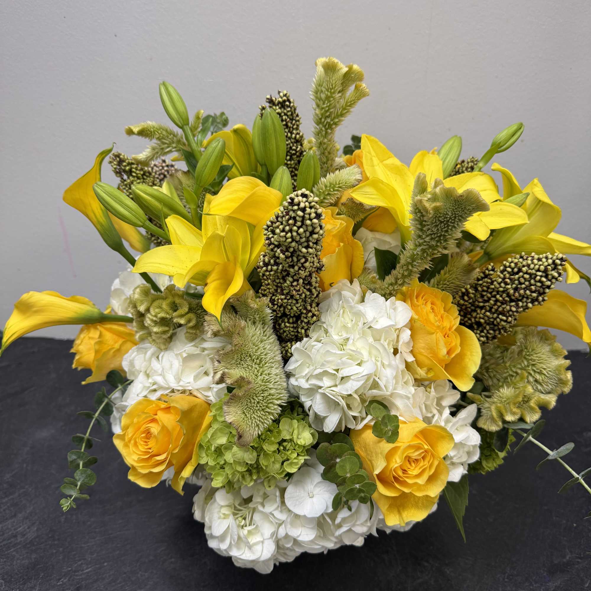 Bright and uplifting, this arrangement combines vibrant yellow calla lilies, golden roses