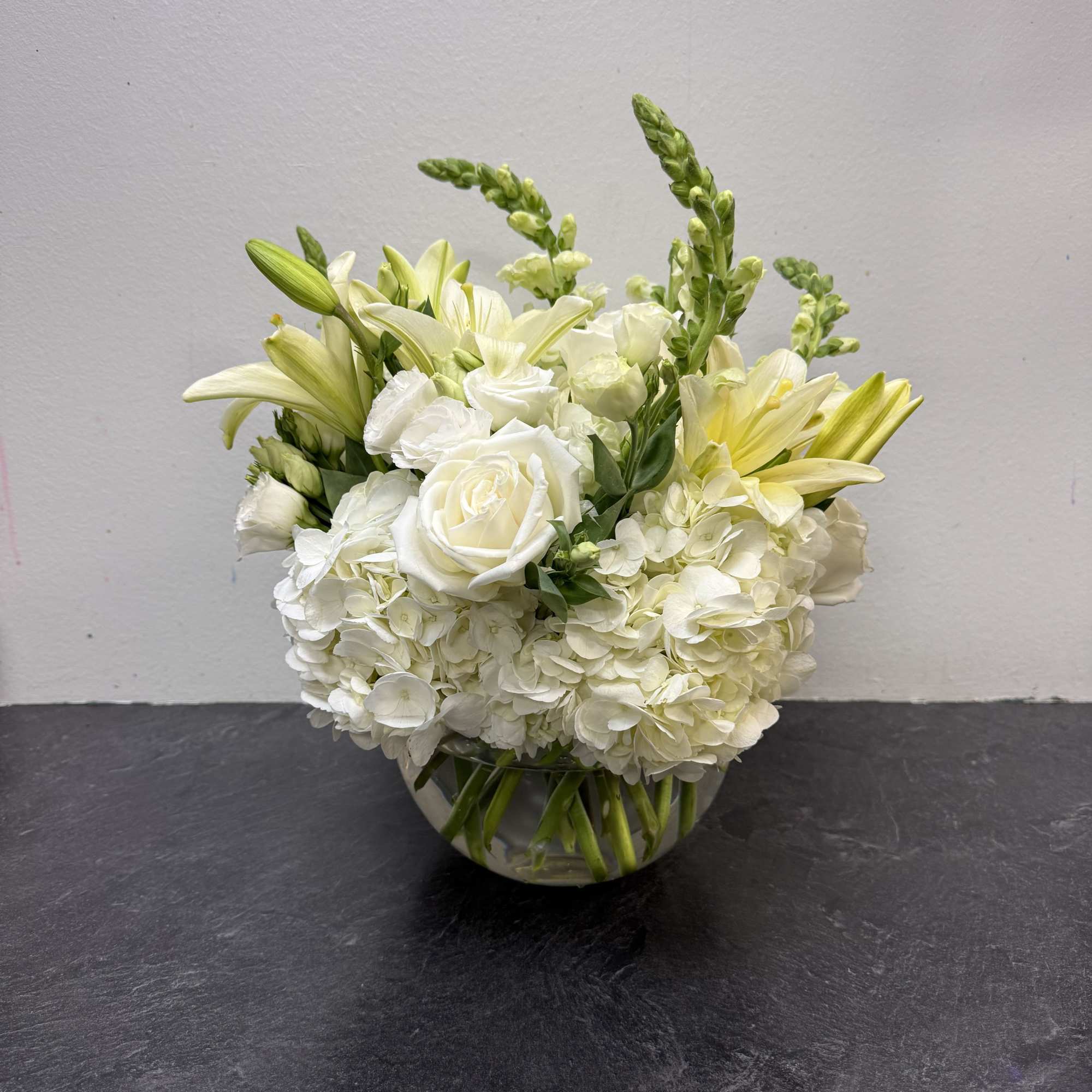 A graceful all-white arrangement featuring lush hydrangeas, classic roses, and elegant lilies