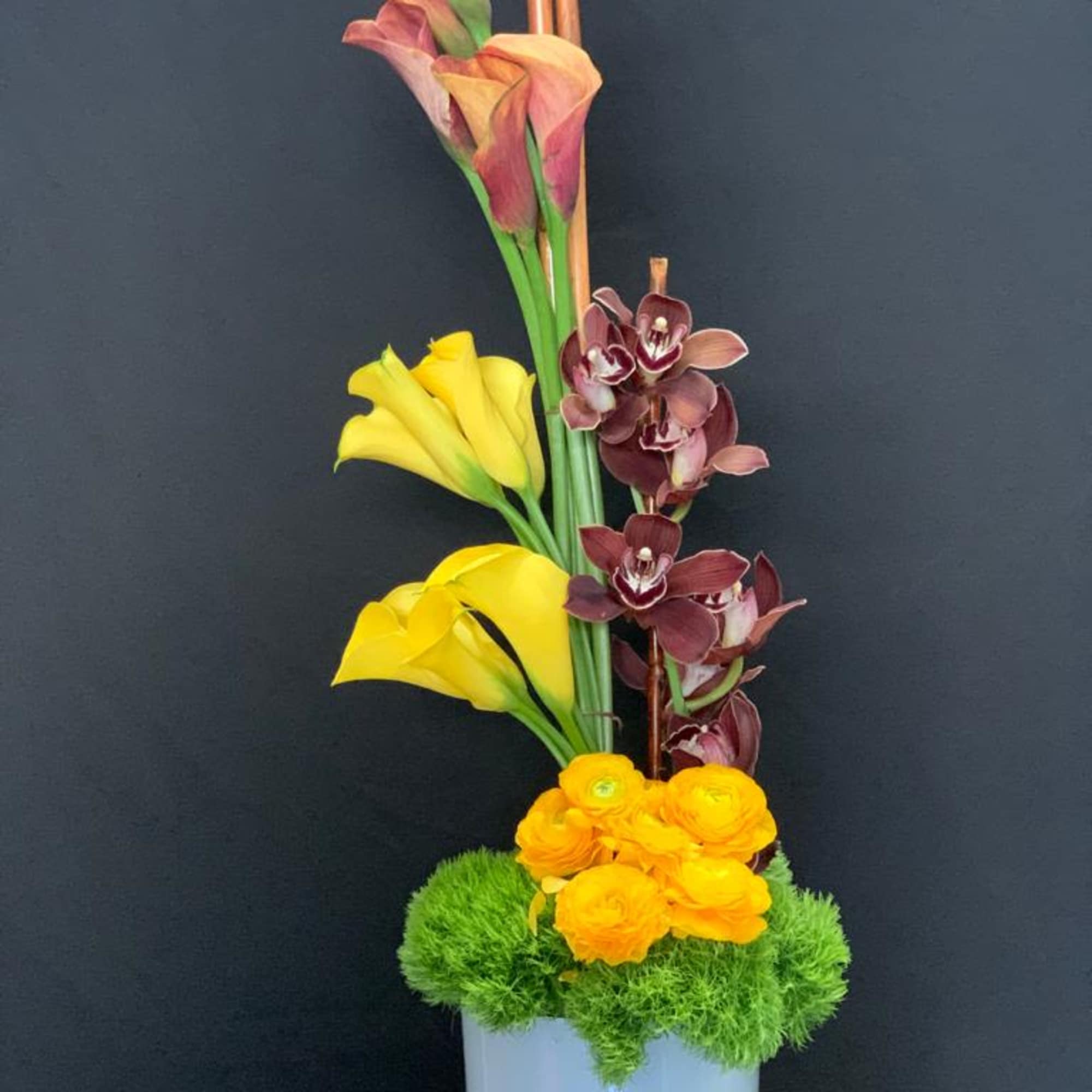Elegant floral arrangement featuring callas, ranunculus, and cymbidium orchids. A stunning blend