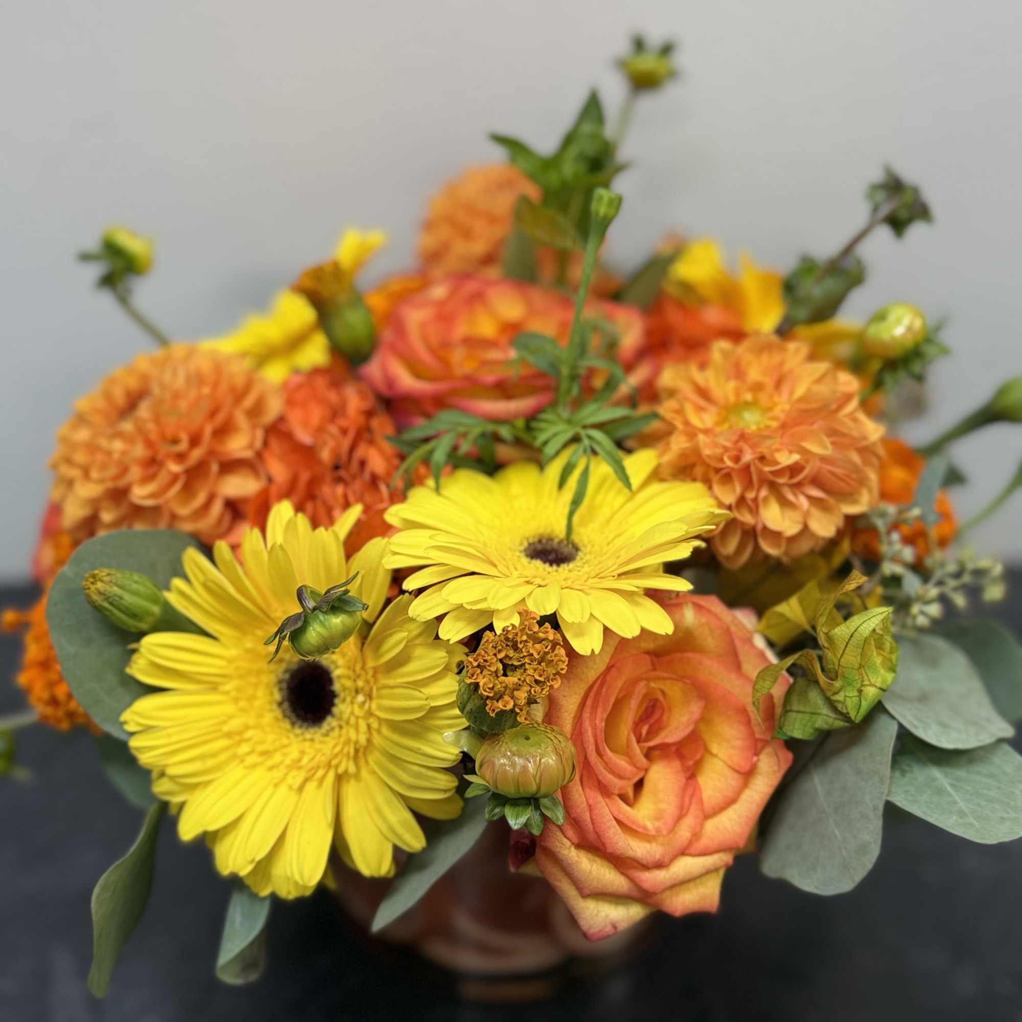 Bright and cheerful, this vibrant arrangement bursts with the warm hues of
