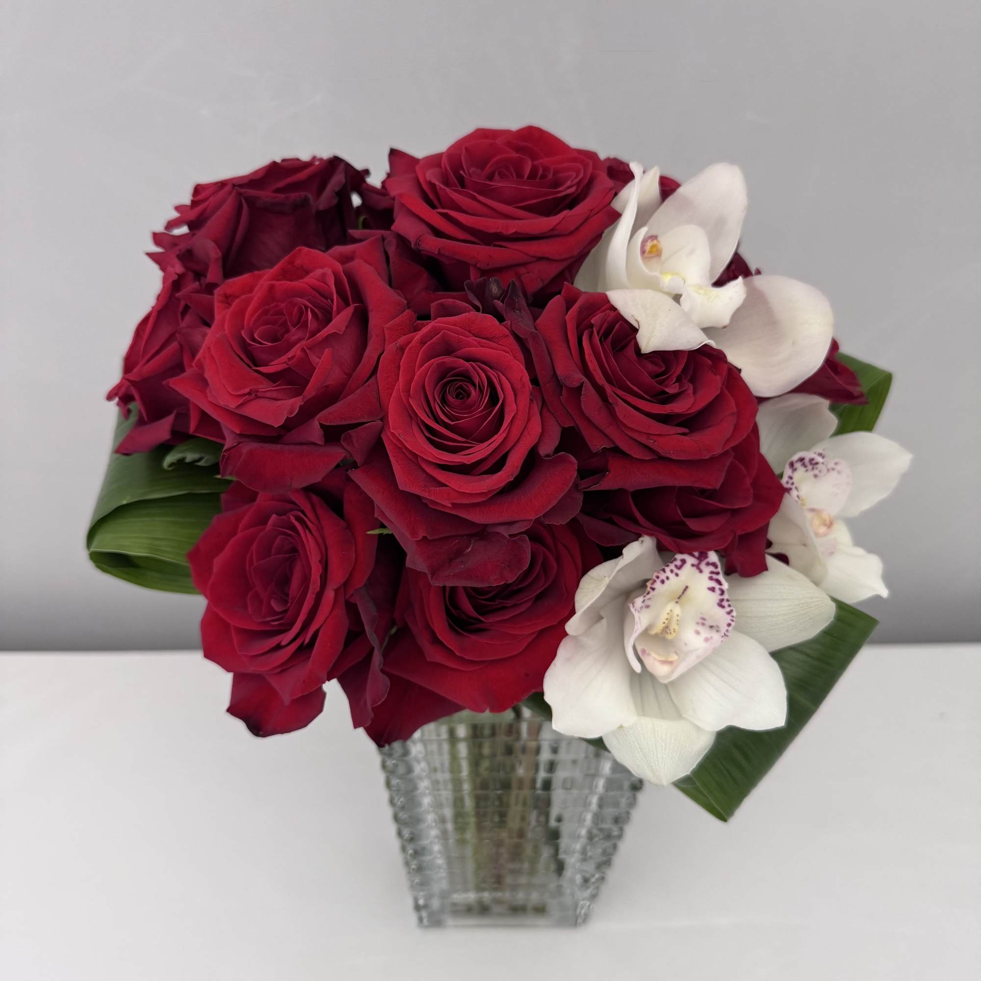 RED LUXE IS AN ARRANGEMENT OF RED ROSES AND CYMBIDUM ORCHIDS DESIGNED
