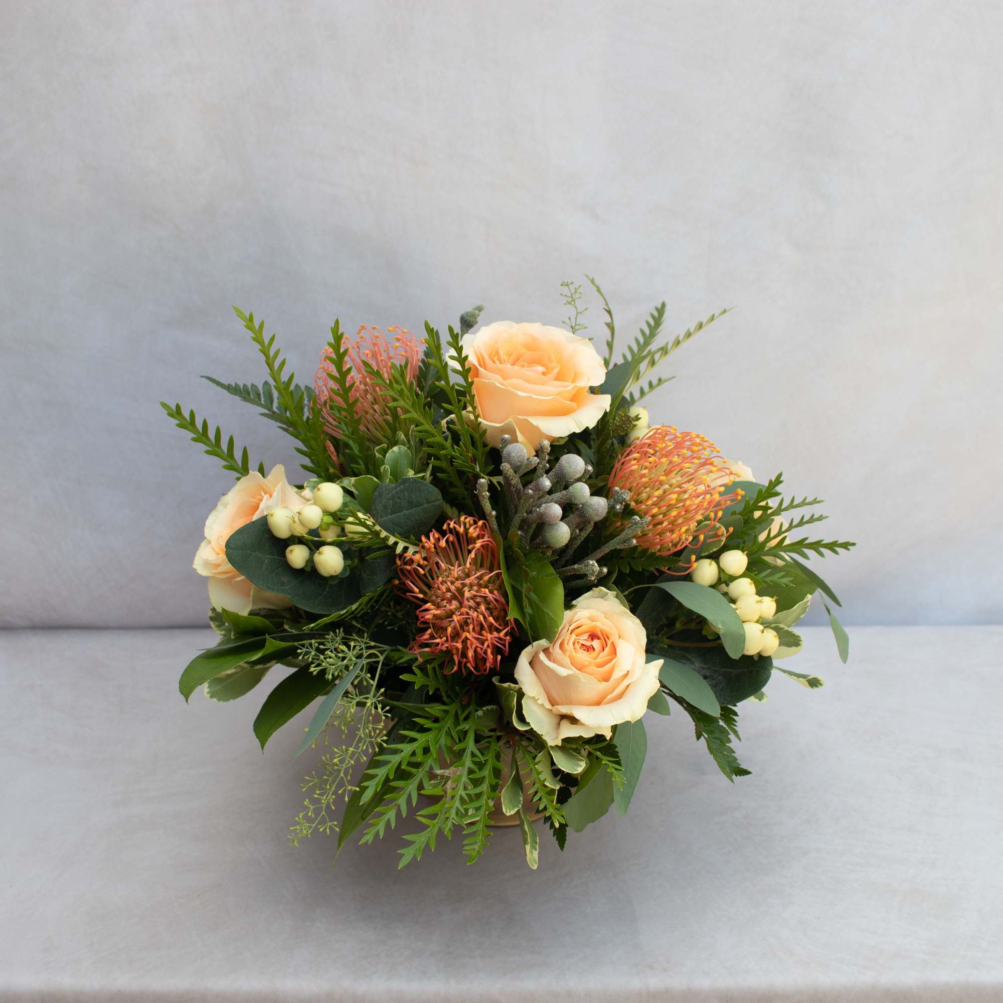 Peach roses, Proteas, berries, mixed with a variety of greenery in a
