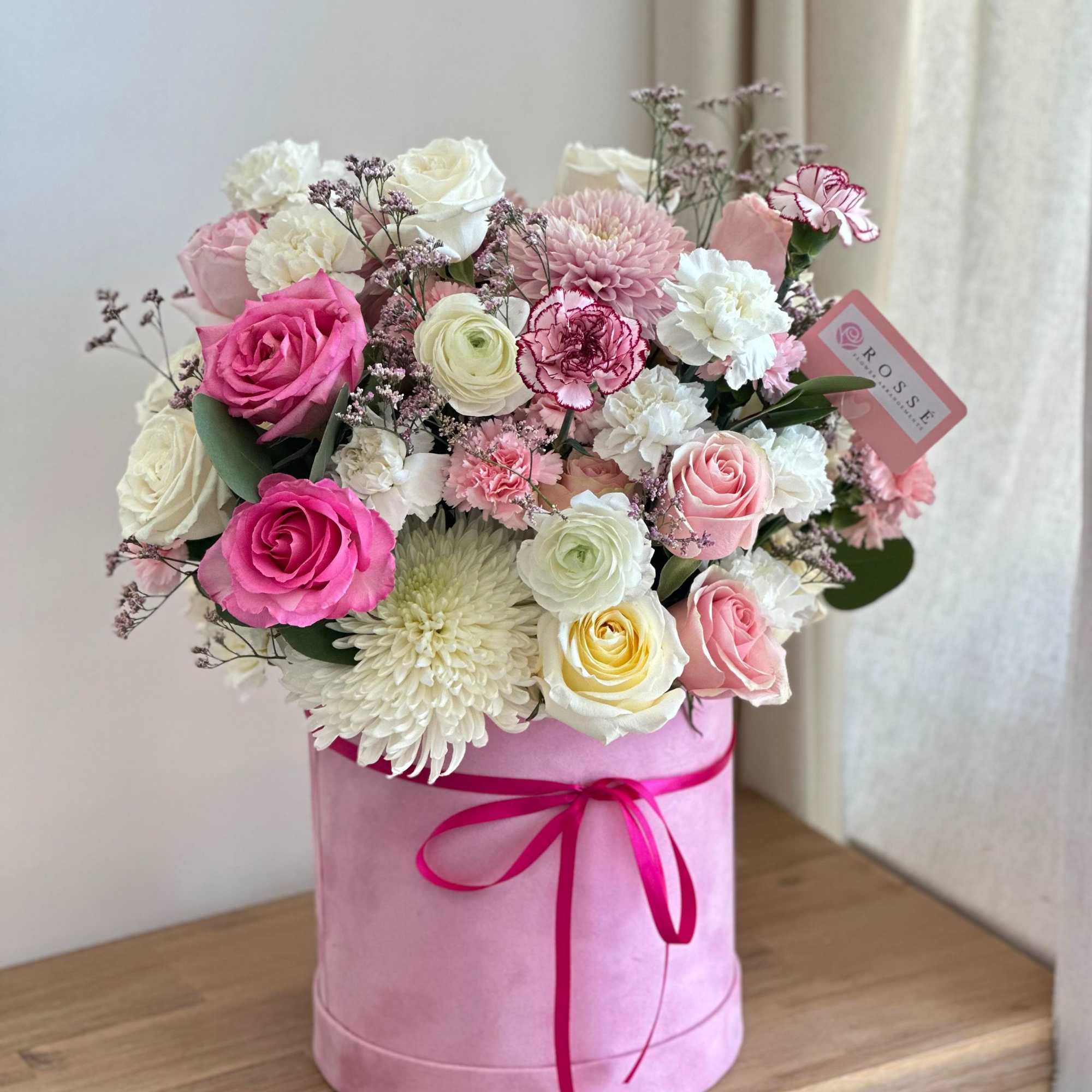 A tall, round pink velvet box filled with pink, light pink, and