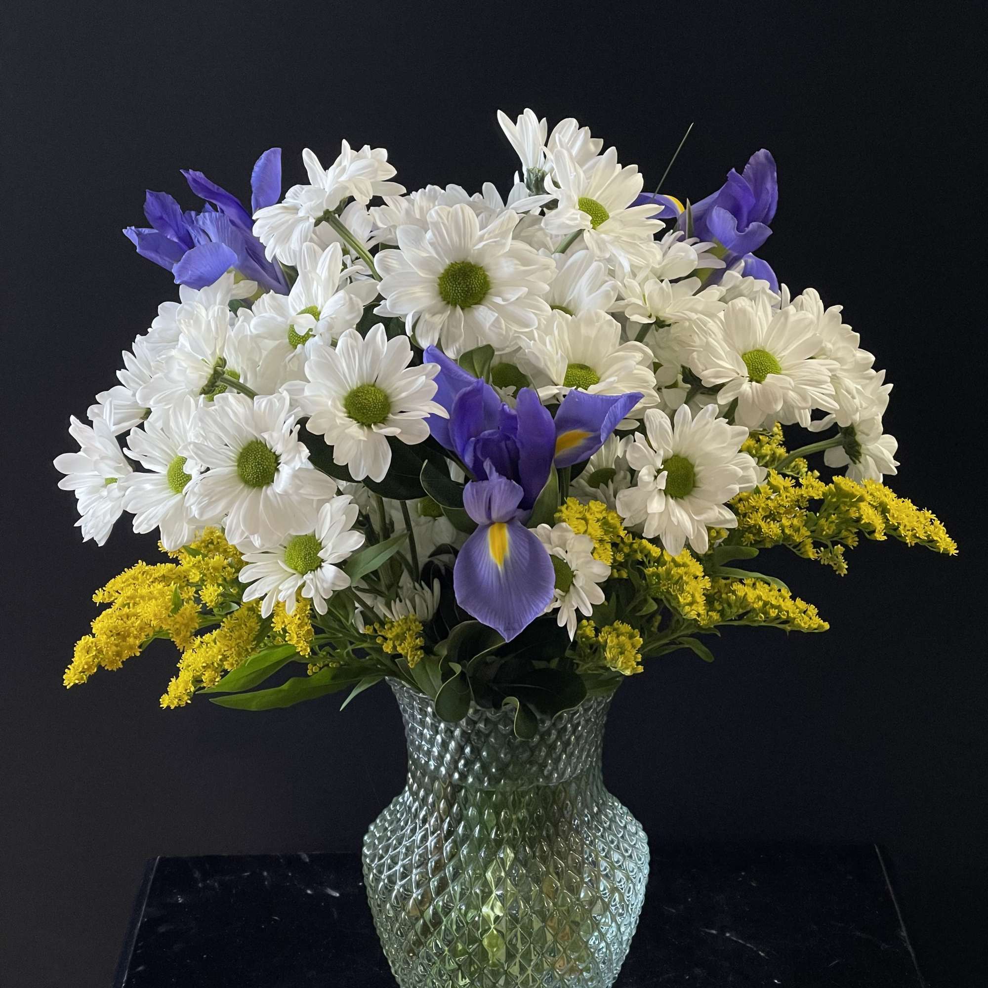 A mint green vase full of daisies and blue iris.