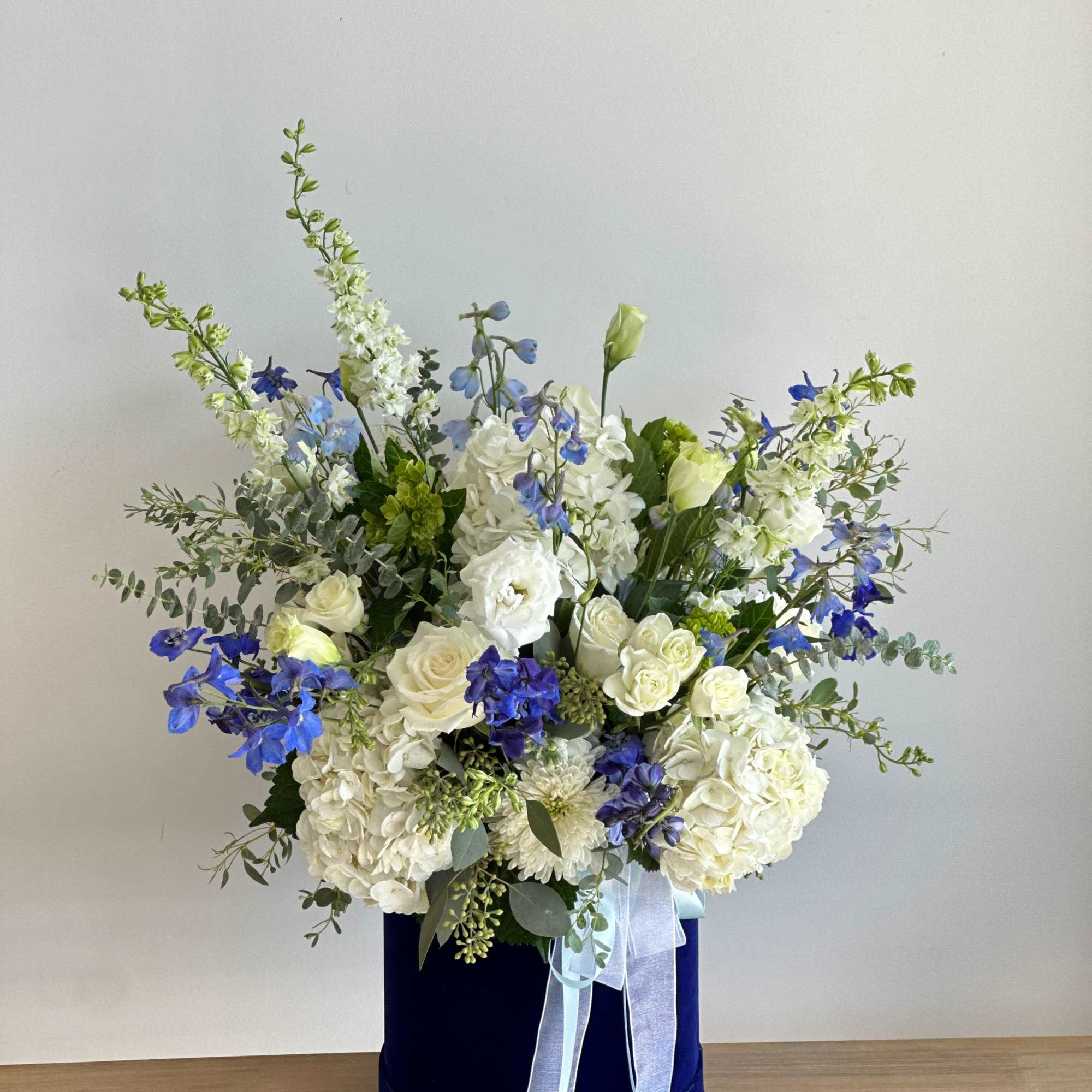 A tall blue velvet cylinder Box filled with a mix of blue