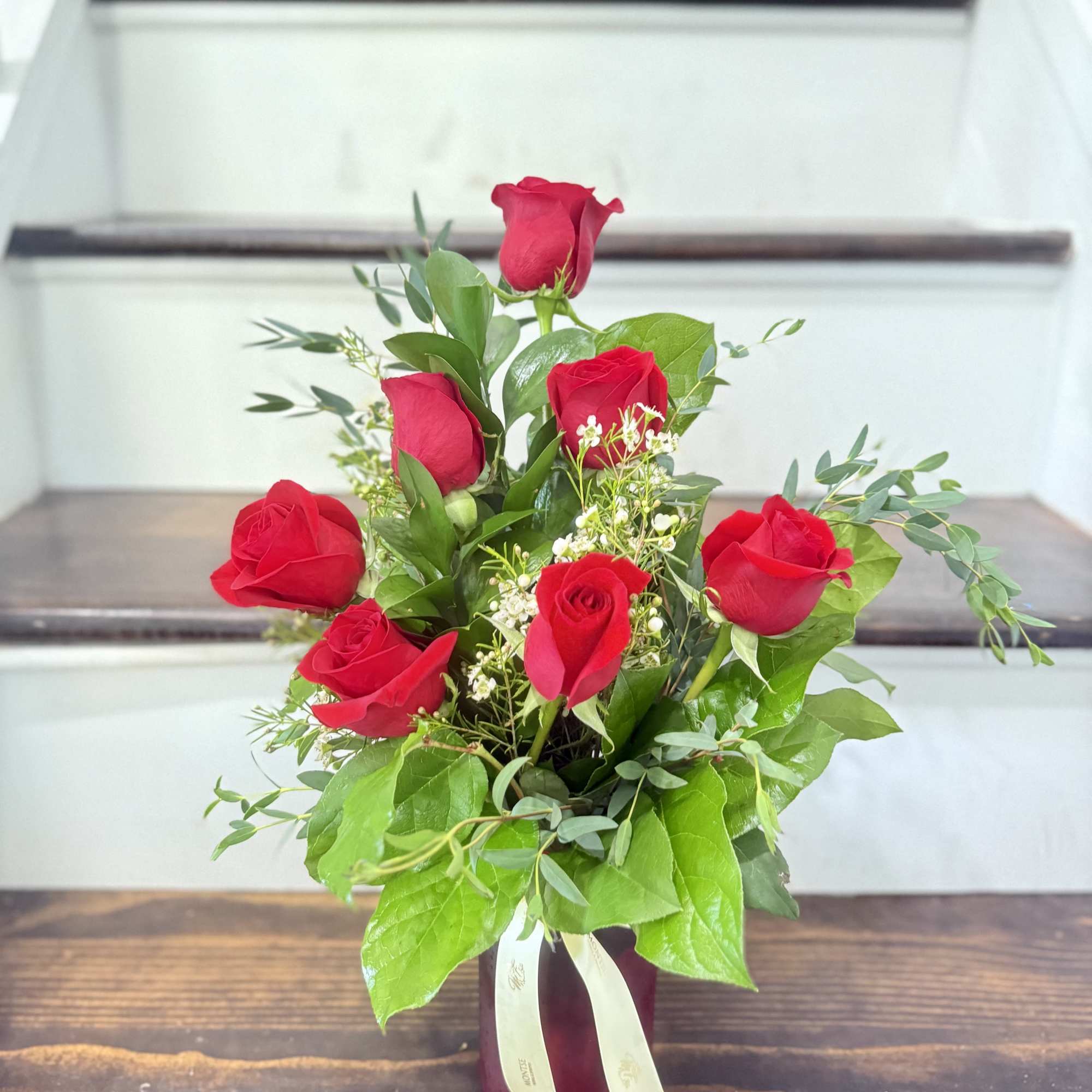 7 red roses in a vase with eucalyptus and wax flowers 
