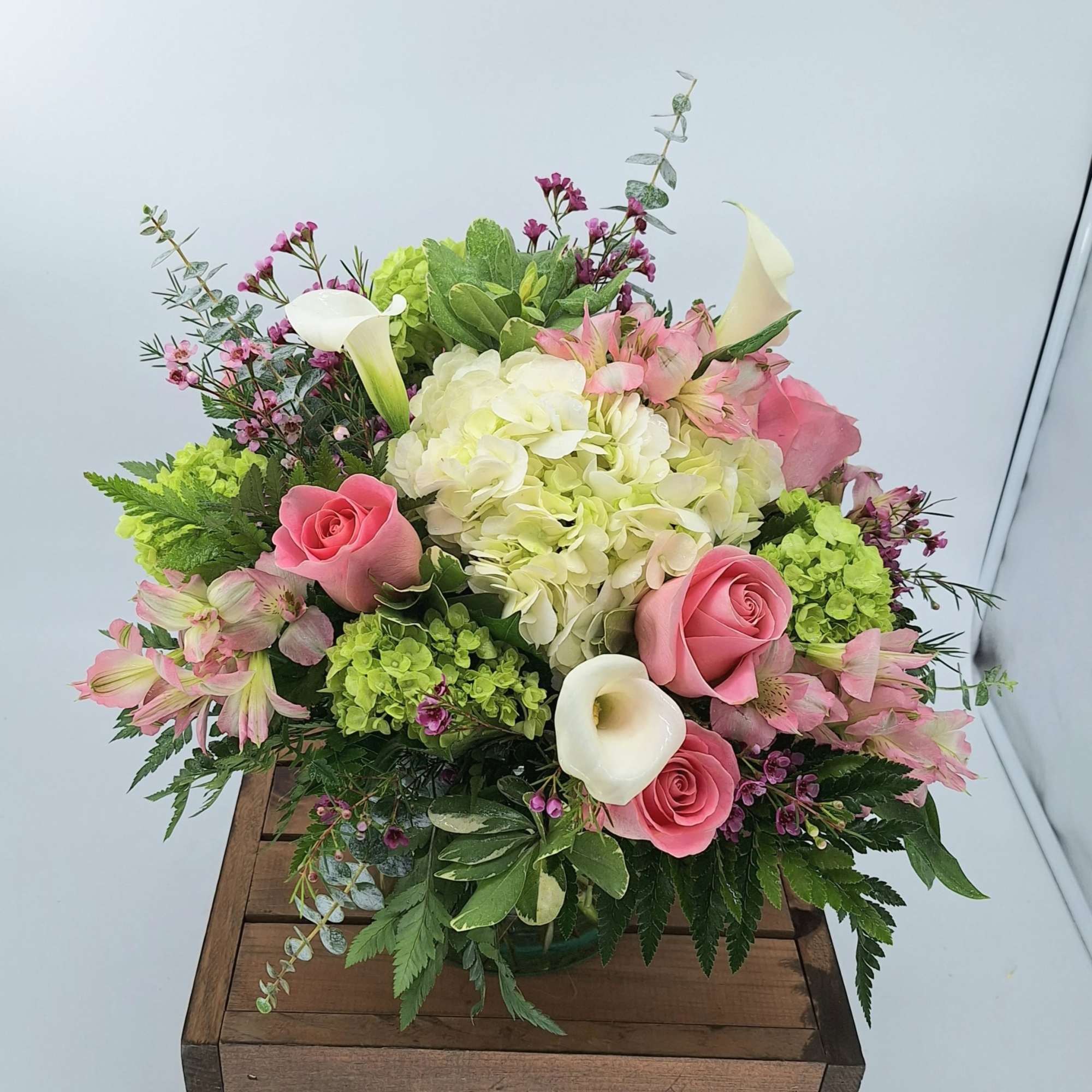 This arrangement includes blush pink Roses, green Hydrangea, white mini callas, wax
