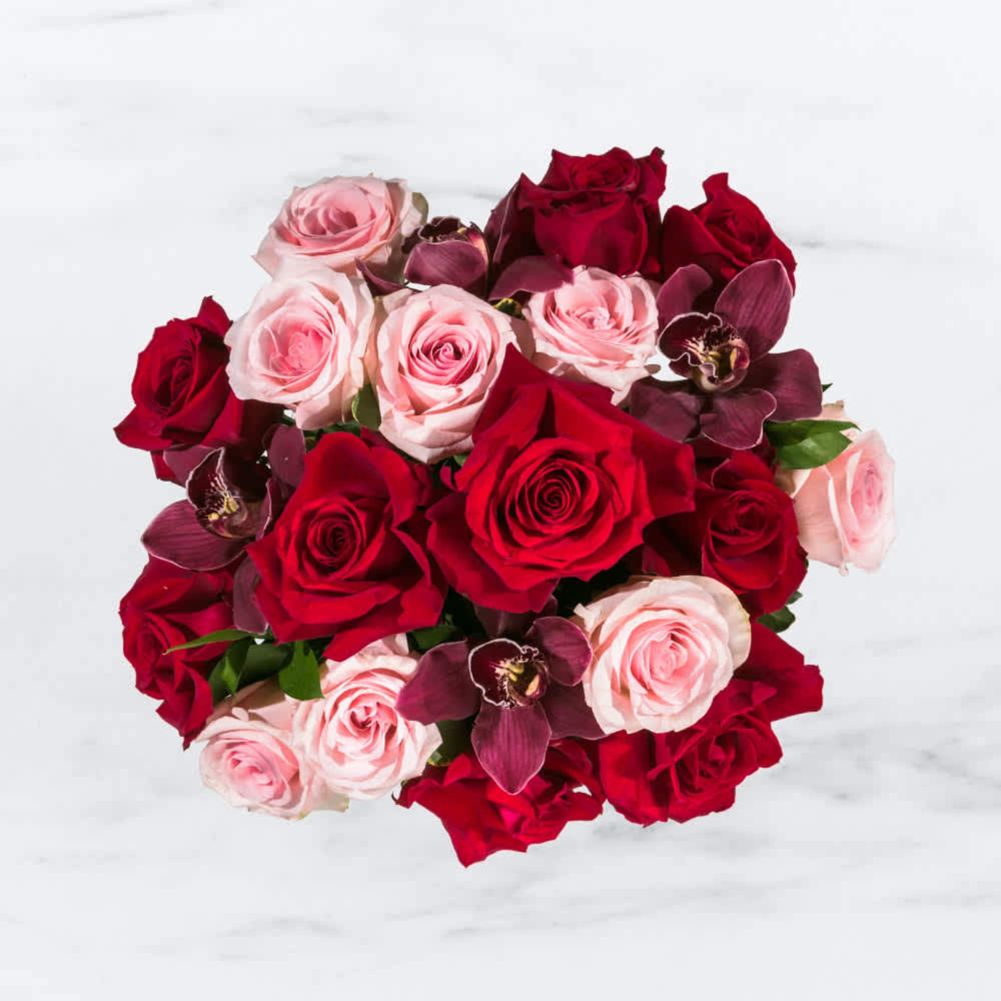 This arrangement includes purple cymbidium orchids, red roses, &amp; pink roses.