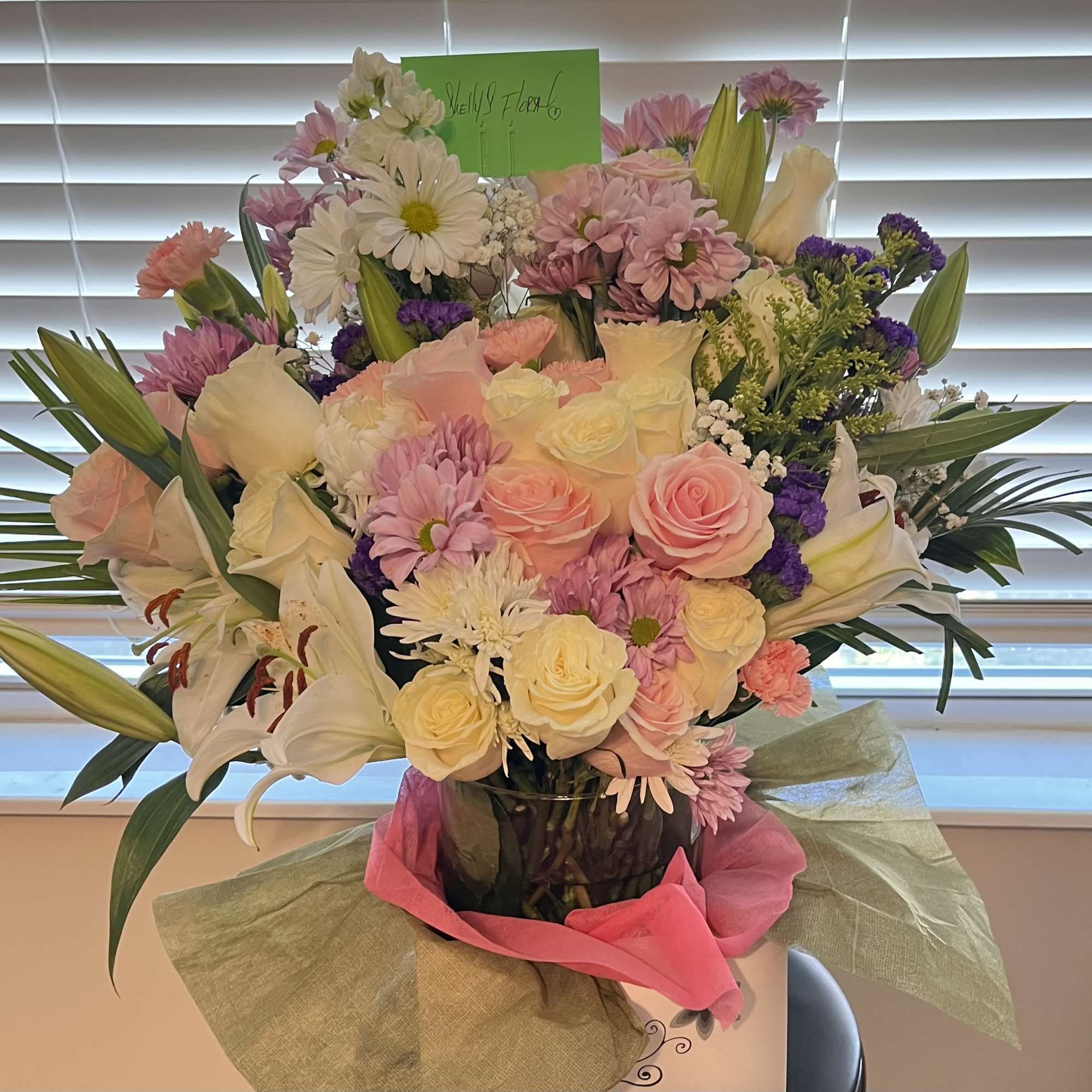 This radiant design features soft pink and ivory roses, cheerful daisies, delicate