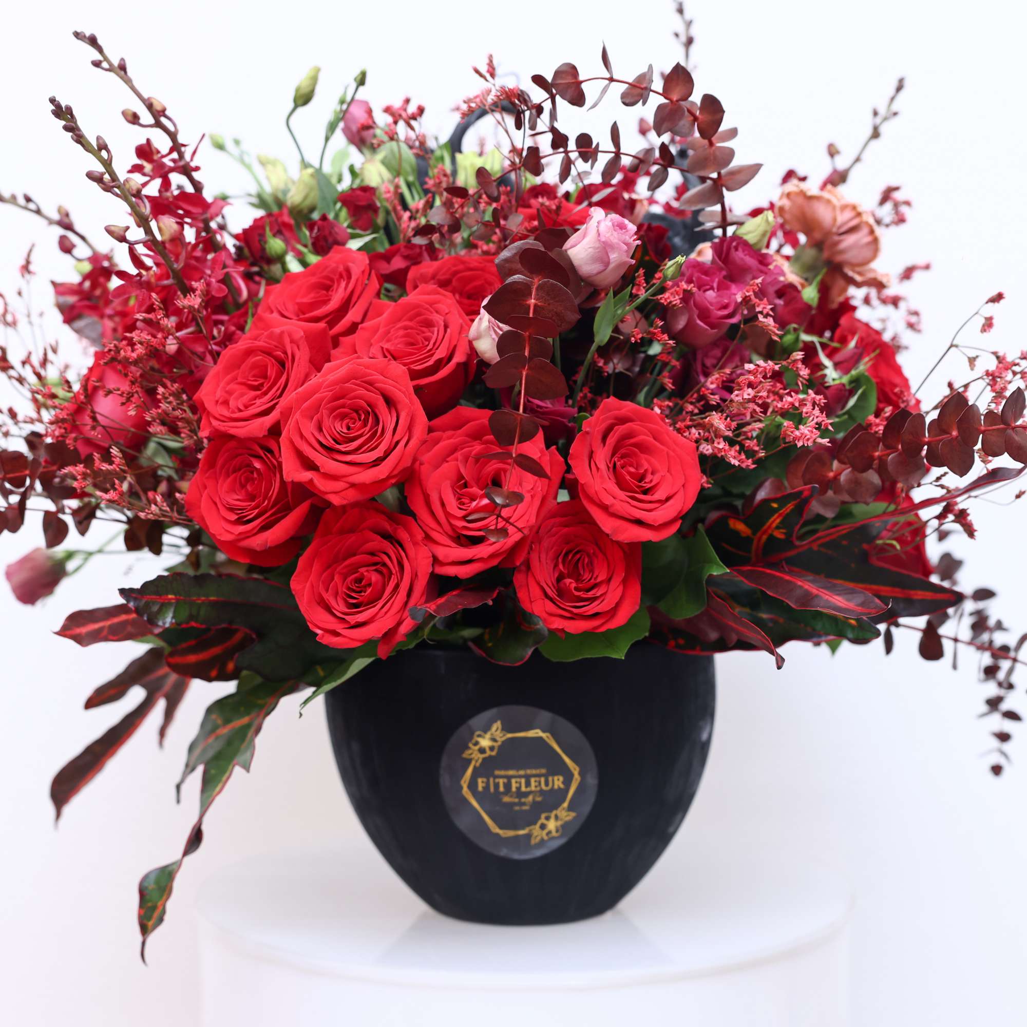 Elegant vibrant round arrangement designed with red roses, carnations, red eucalyptus, spray