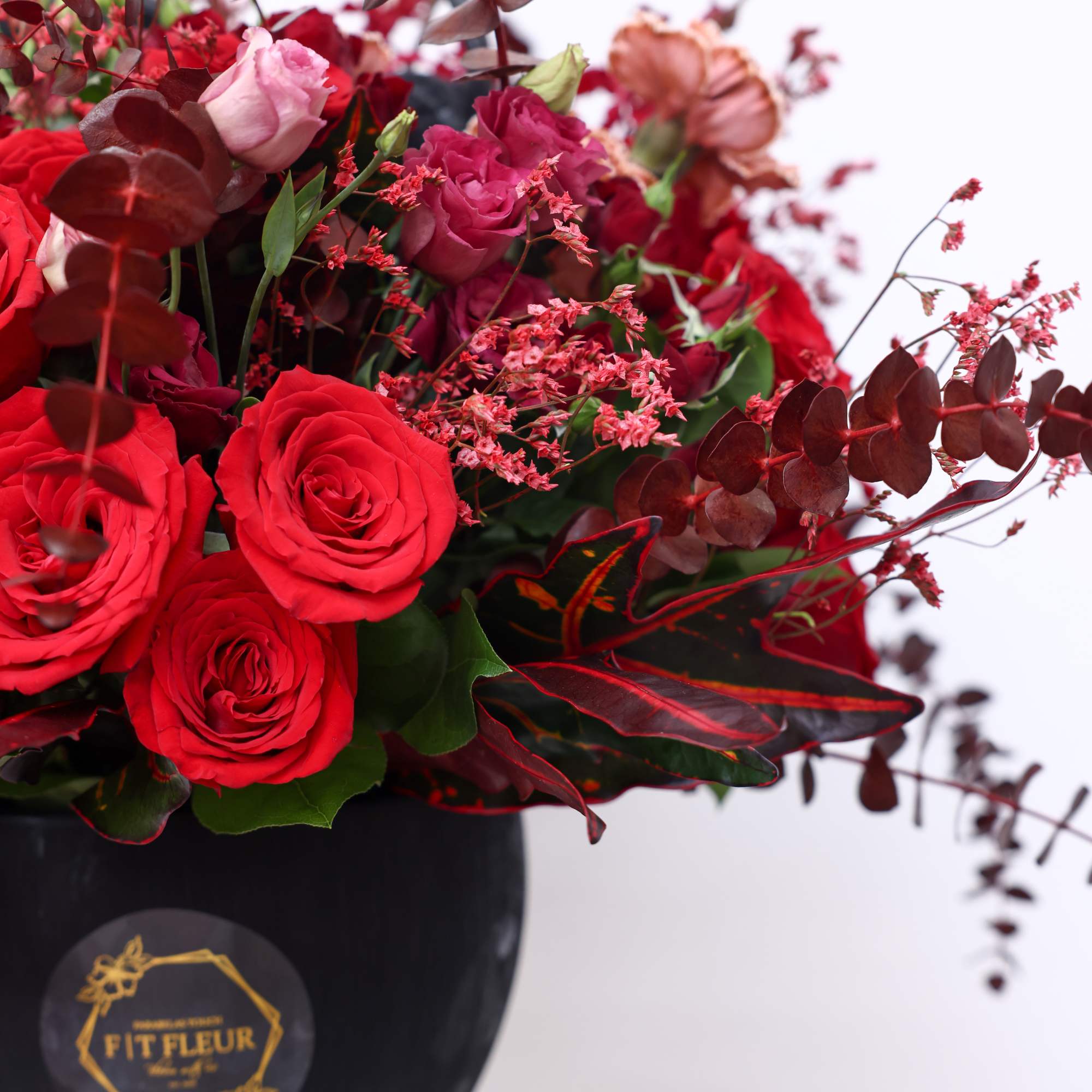 Elegant vibrant round arrangement designed with red roses, carnations, red eucalyptus, spray