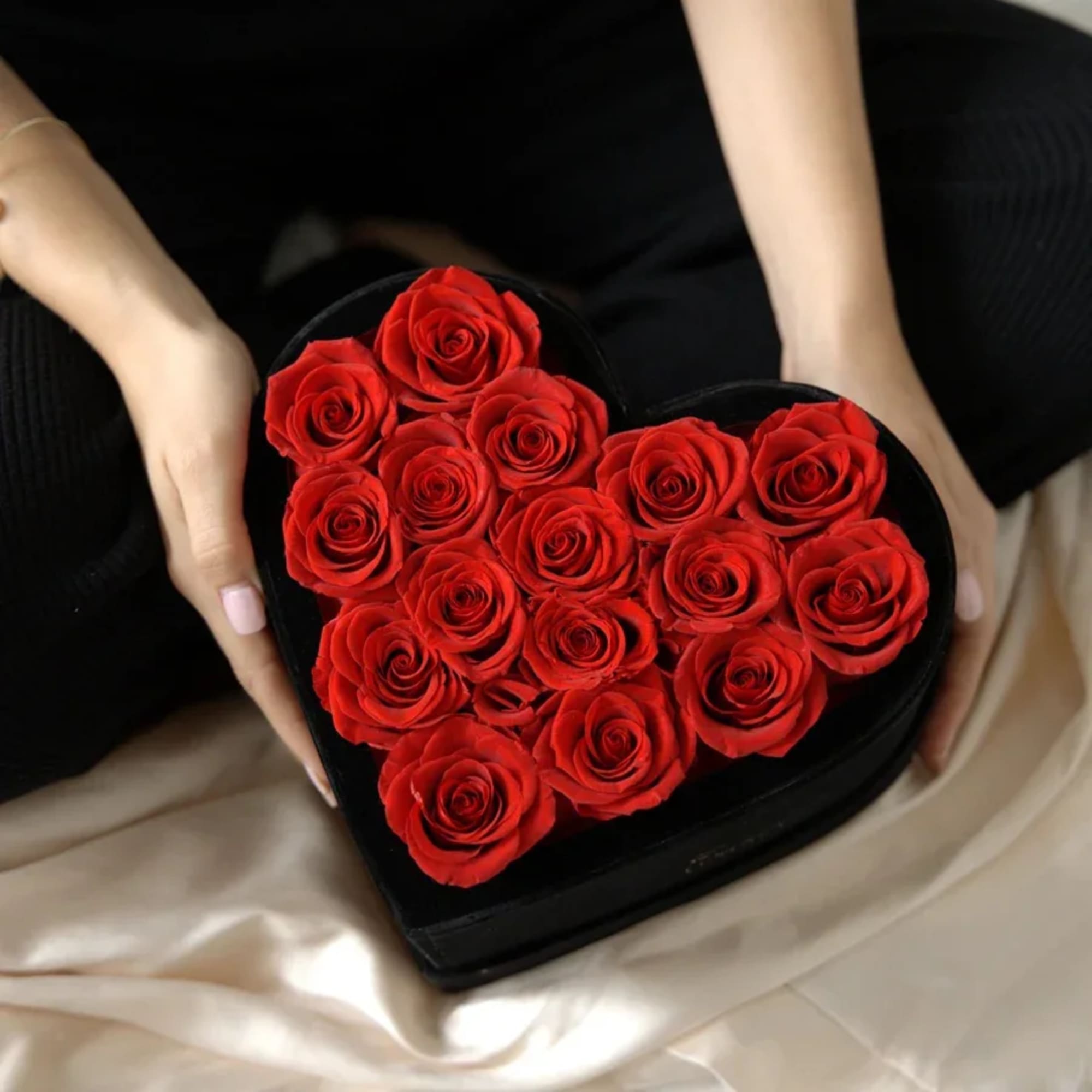 A luxurious black heart-shaped box filled with vibrant, hand-picked red roses. Available