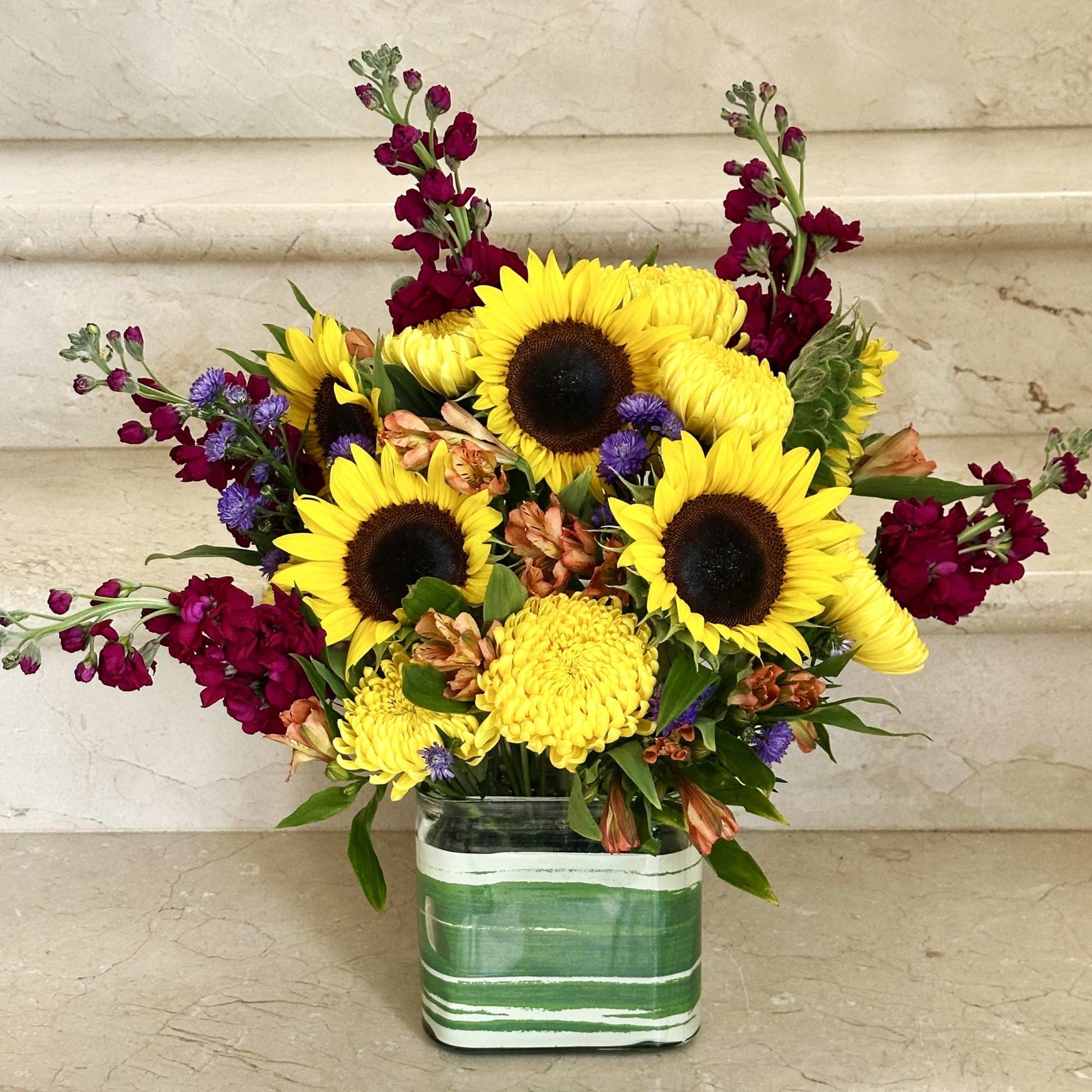 A cheerful mix of sunflowers, burgundy snapdragons, yellow mums, and other seasonal A cheerful mix of sunflowers, burgundy snapdragons, yellow mums, and other seasonal
