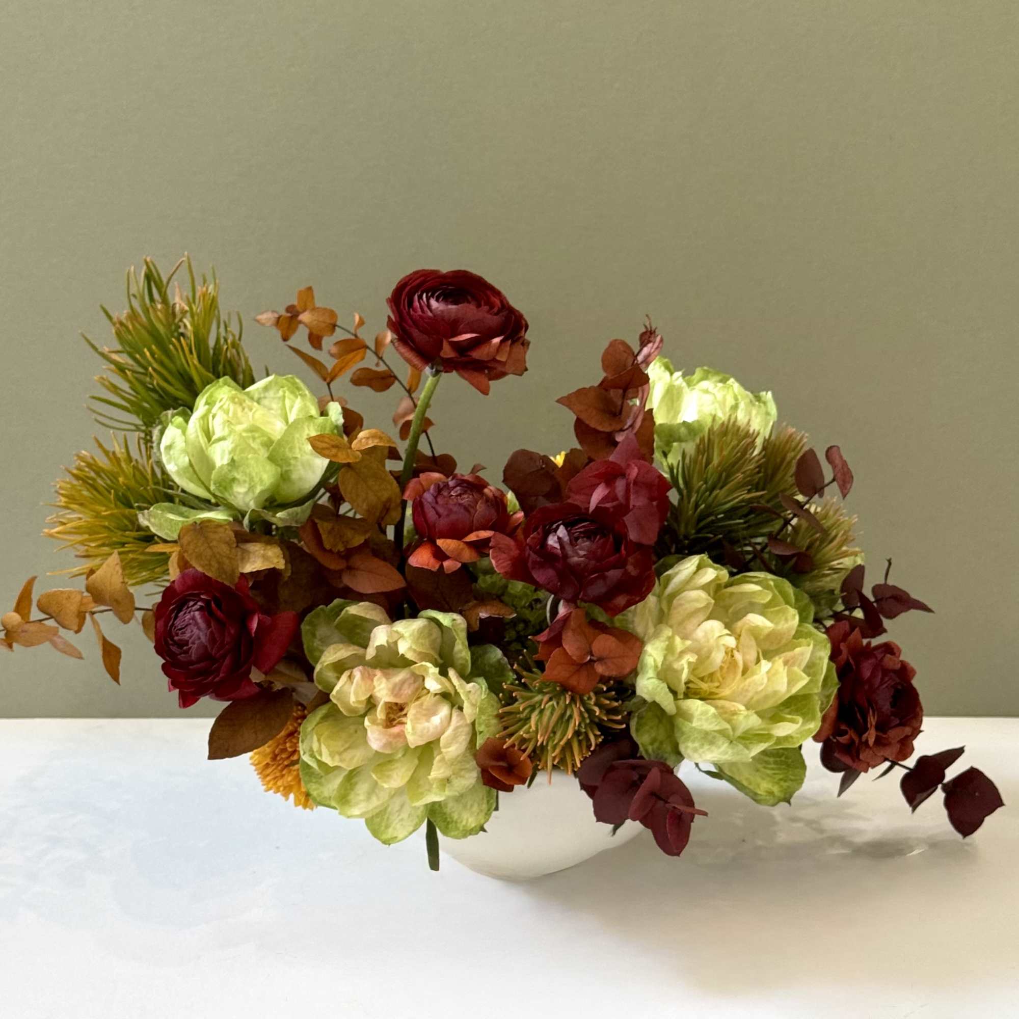 A striking fall composition blending deep burgundy ranunculus, warm amber foliage, and