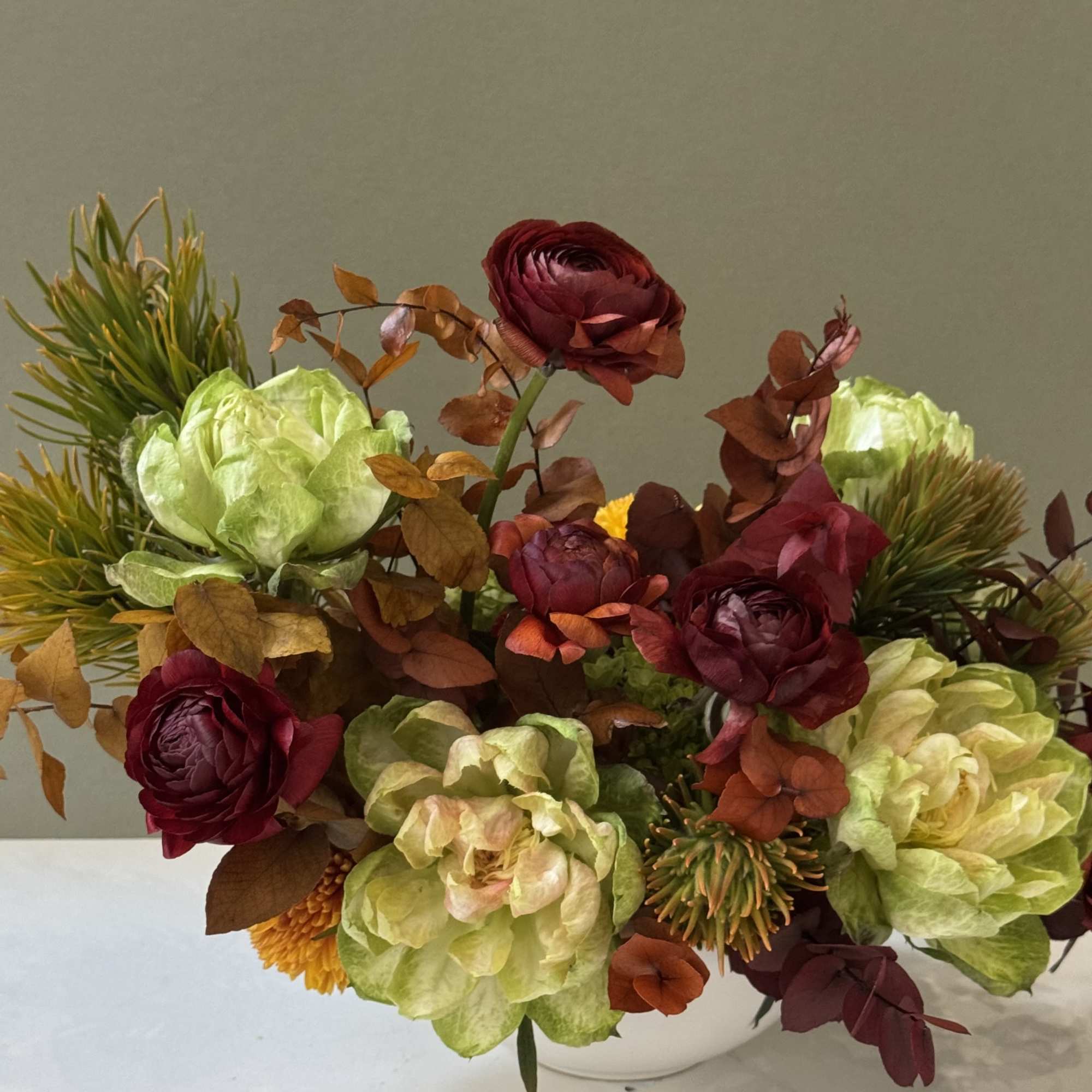 A striking fall composition blending deep burgundy ranunculus, warm amber foliage, and