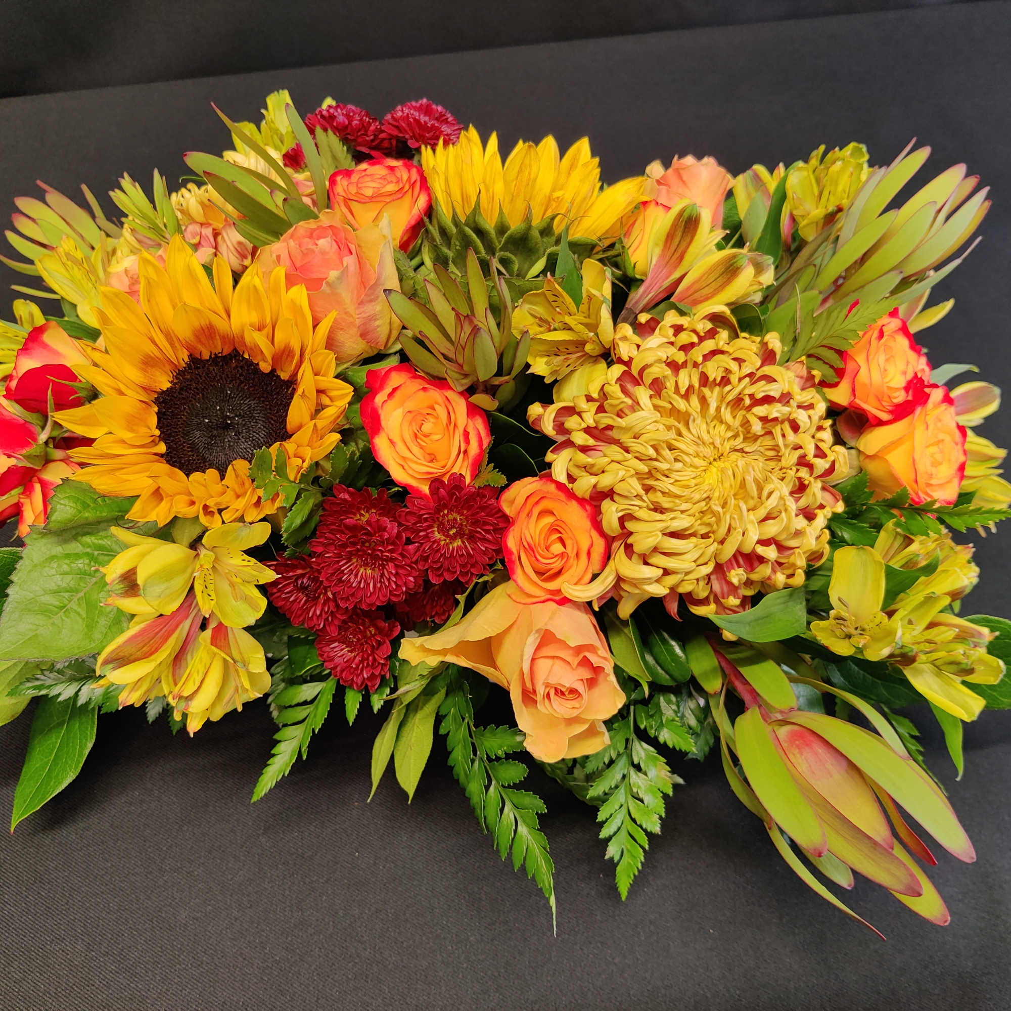 A thickly arranged centerpiece of fall flowers in a low design dish.
