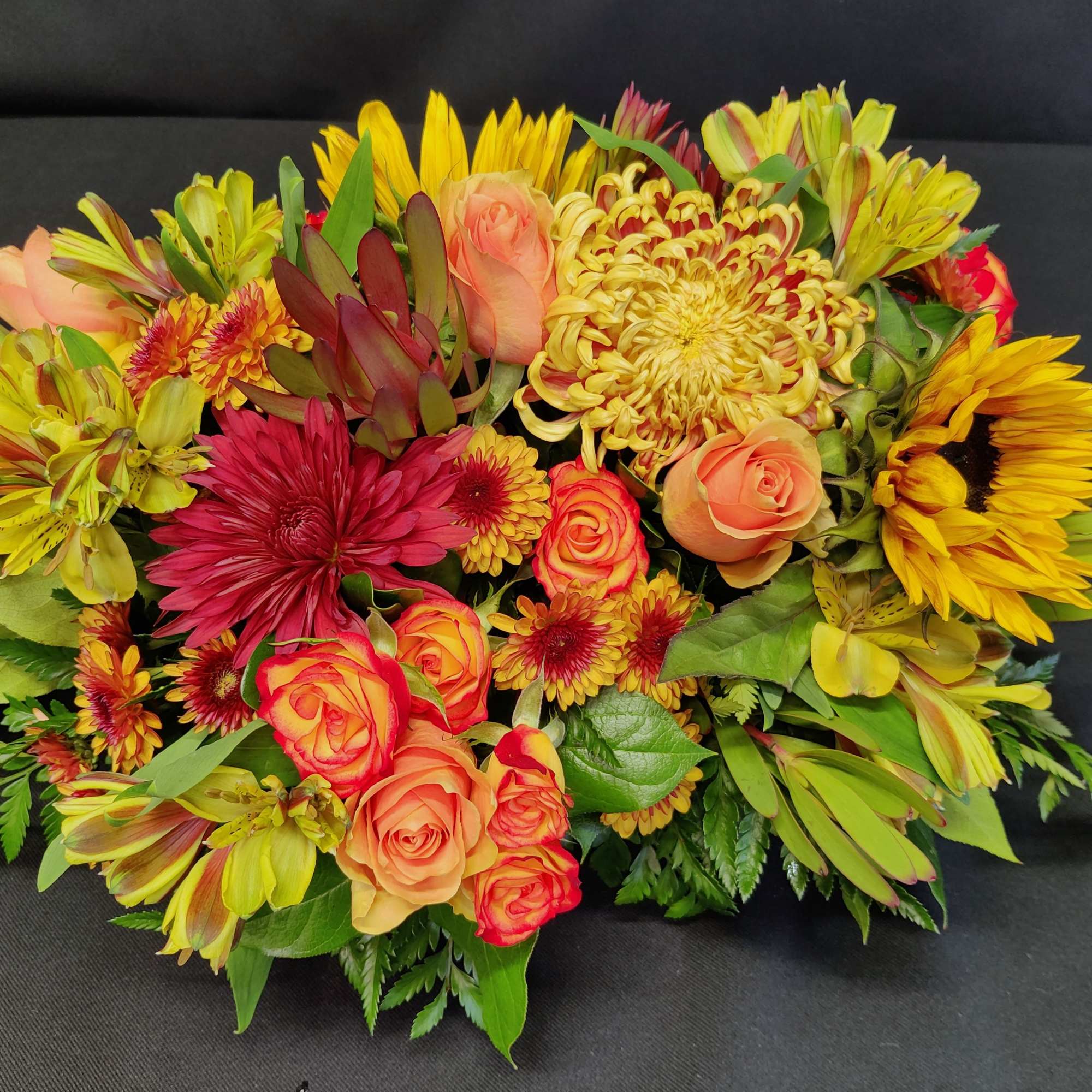 A thickly arranged centerpiece of fall flowers in a low design dish.