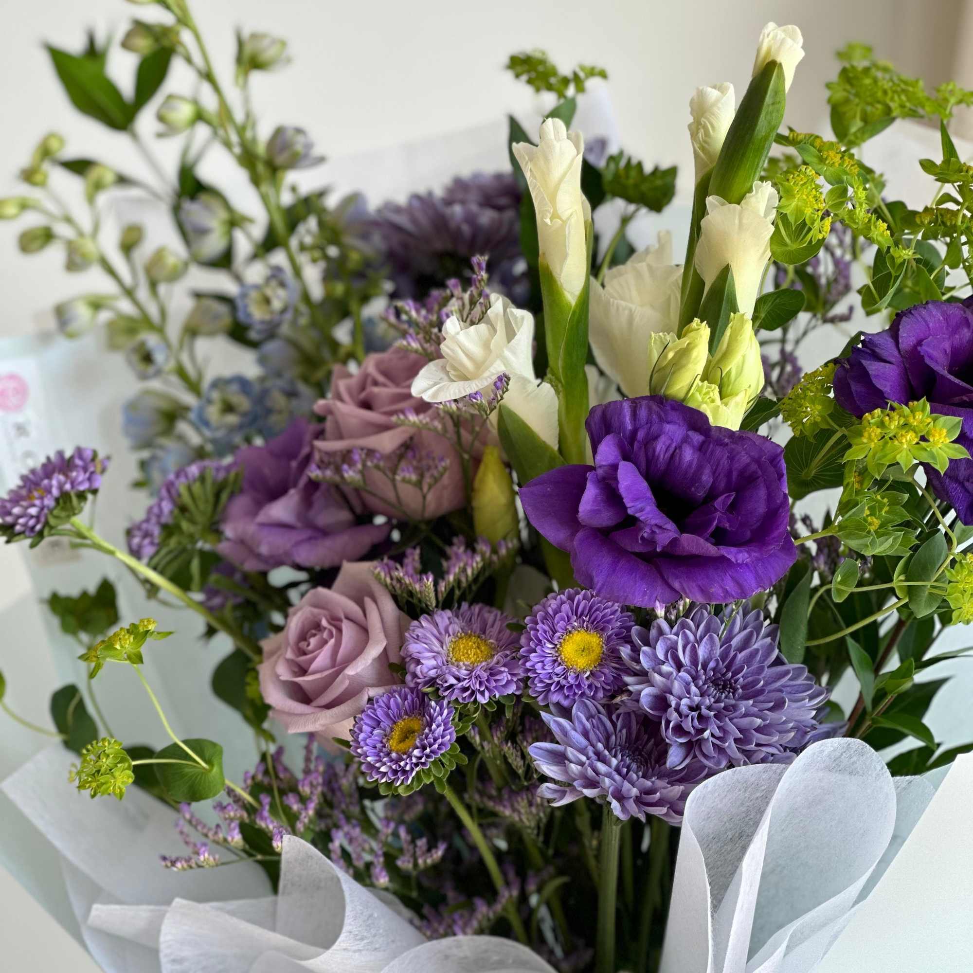 A front-facing bouquet with white, green, purple, and light blue flowers, wrapped