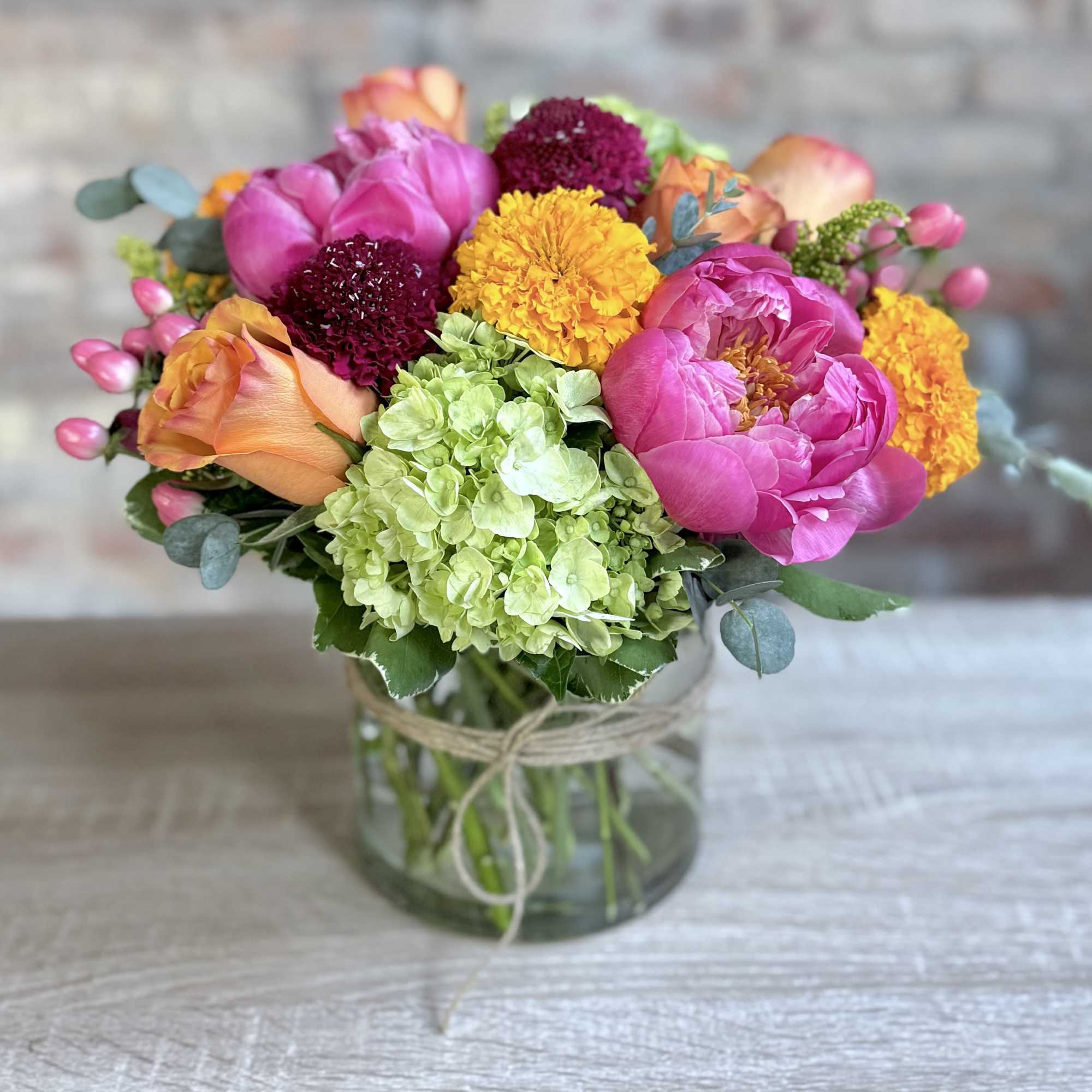A low and wide cylinder vase filled with bright coral, green and A low and wide cylinder vase filled with bright coral, green and
