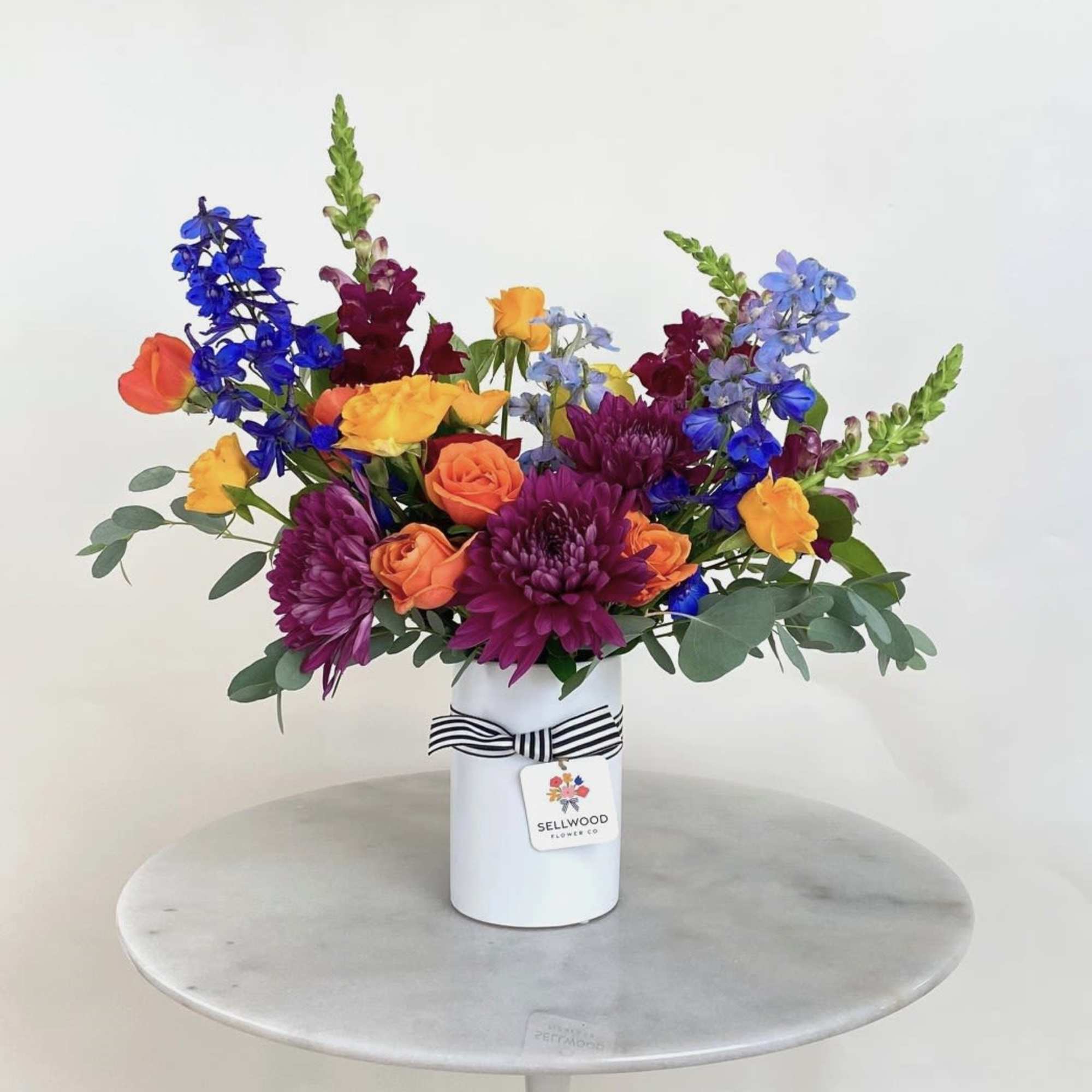 This arrangement bursts with vibrant, rainbow-hued flowers. Each bloom is thoughtfully chosen