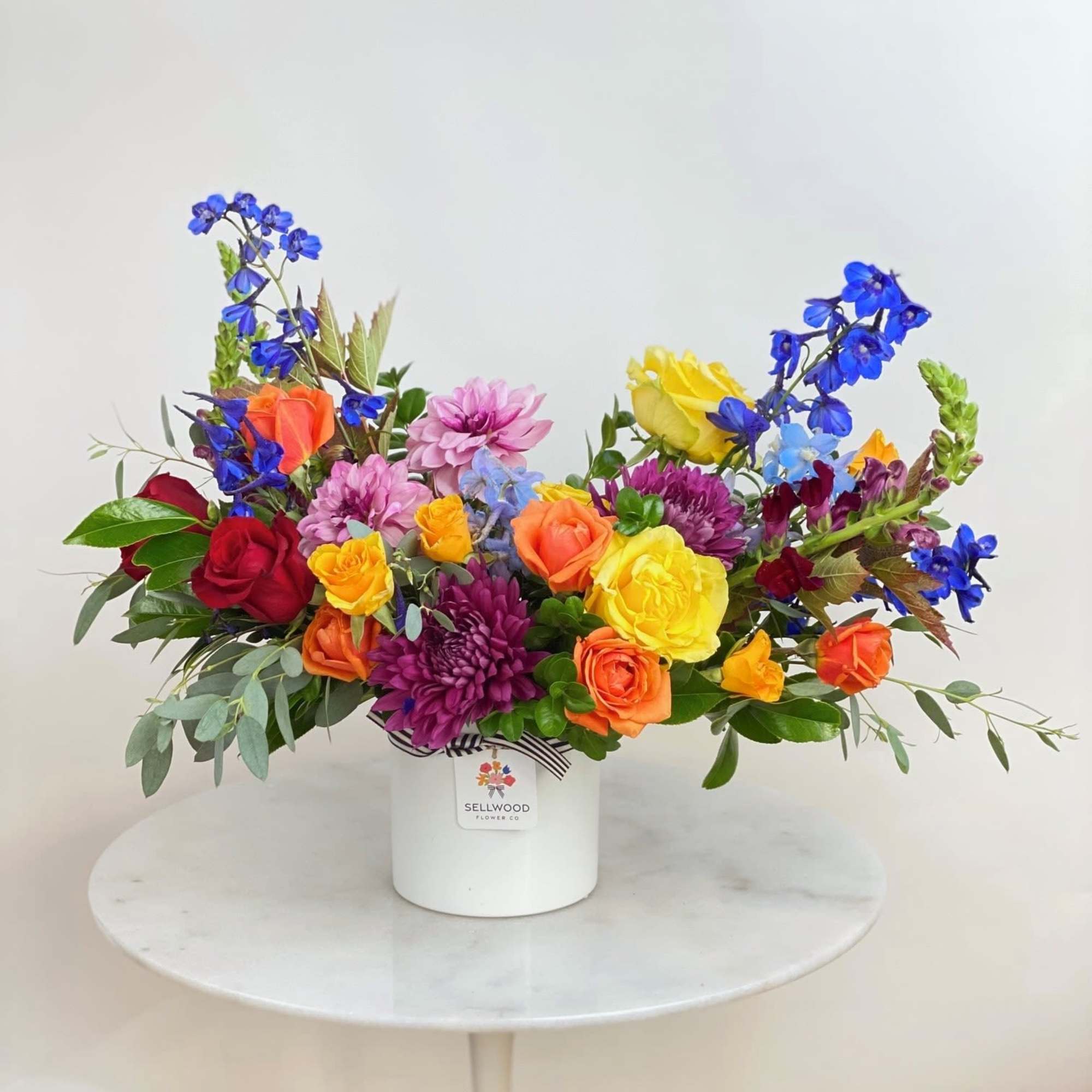 This arrangement bursts with vibrant, rainbow-hued flowers. Each bloom is thoughtfully chosen