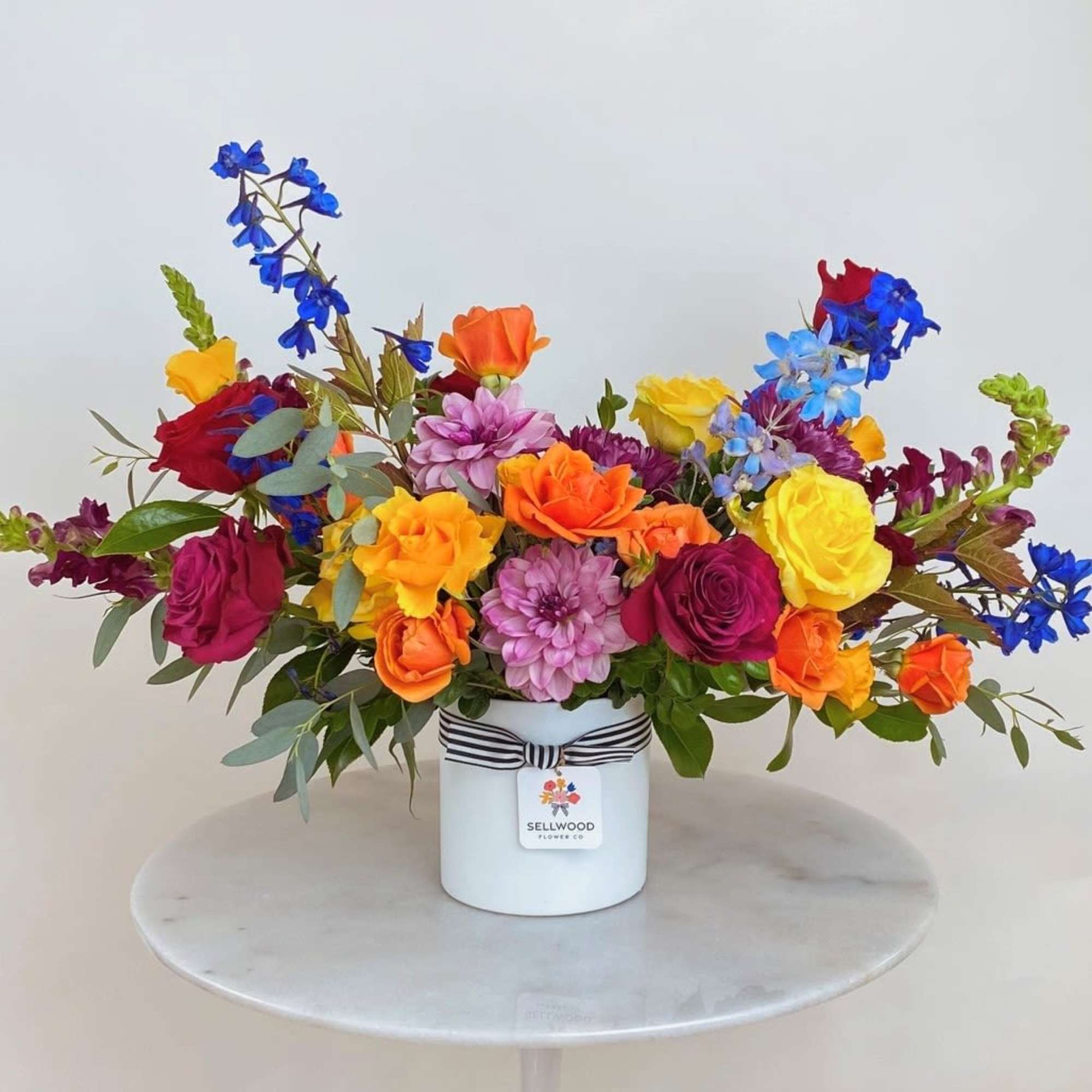 This arrangement bursts with vibrant, rainbow-hued flowers. Each bloom is thoughtfully chosen